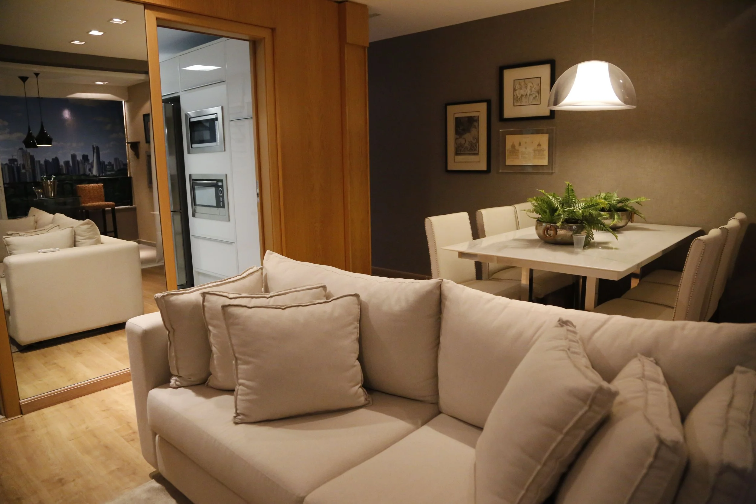 Living room with white sofa, beige chairs, wall art, dining table with plants, and a pendant lamp.