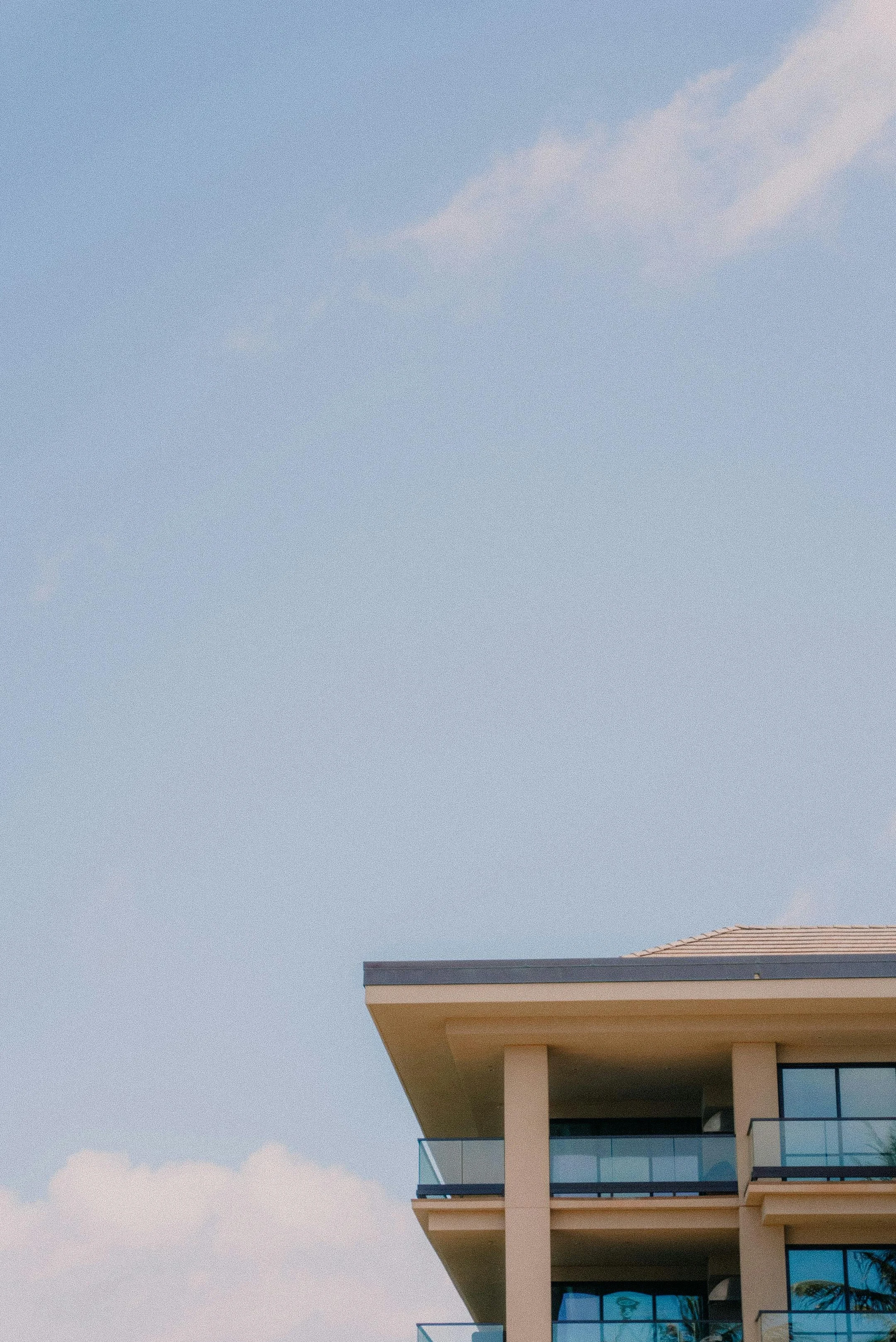 A modern multi-story building with large glass windows and balconies set against a blue sky with some clouds.