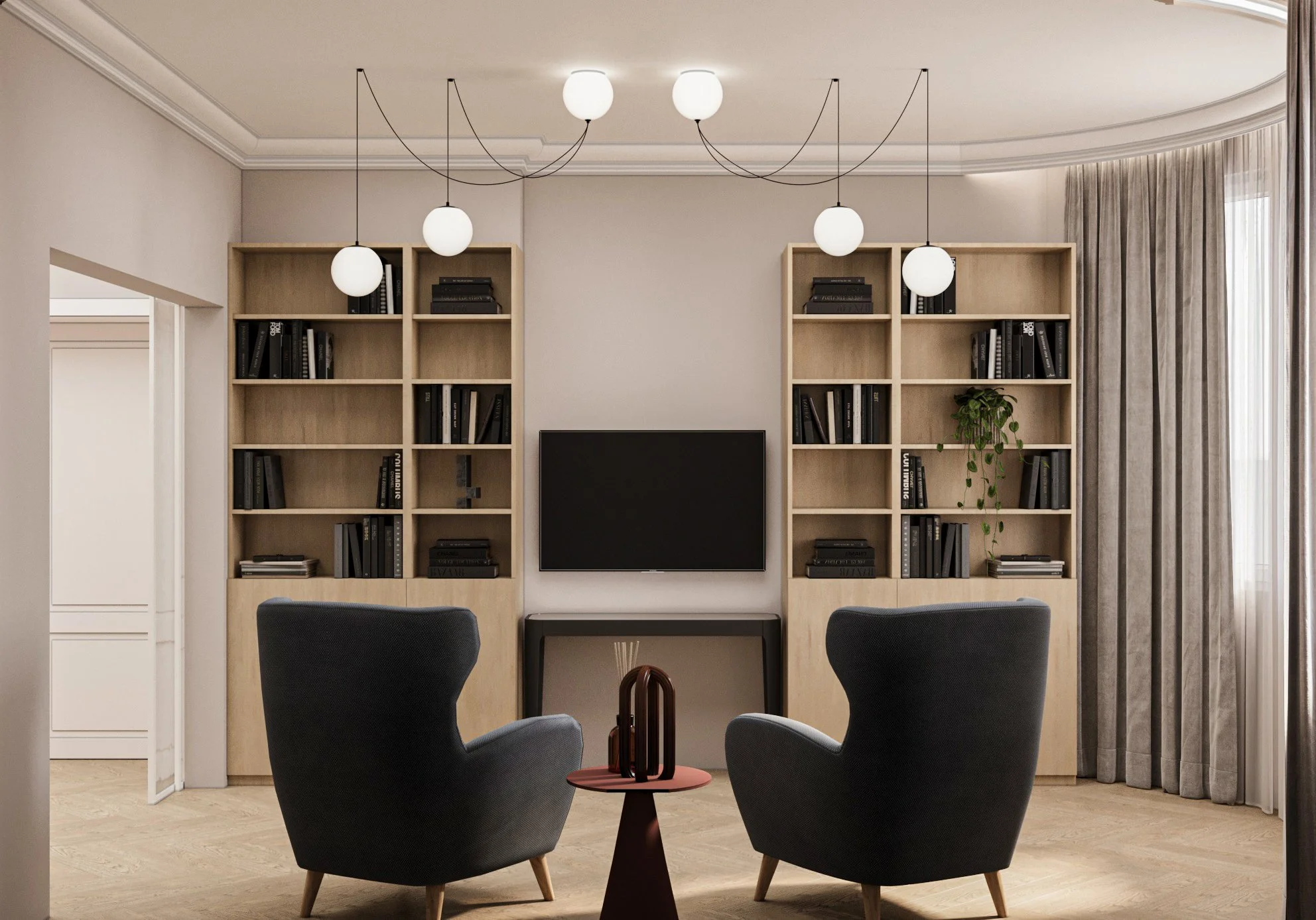 Modern living room with two black armchairs facing a wall-mounted flat-screen TV, flanked by built-in wooden bookshelves. A small round side table with decorative objects is between the chairs. The room has light-colored walls, beige curtains, and a 