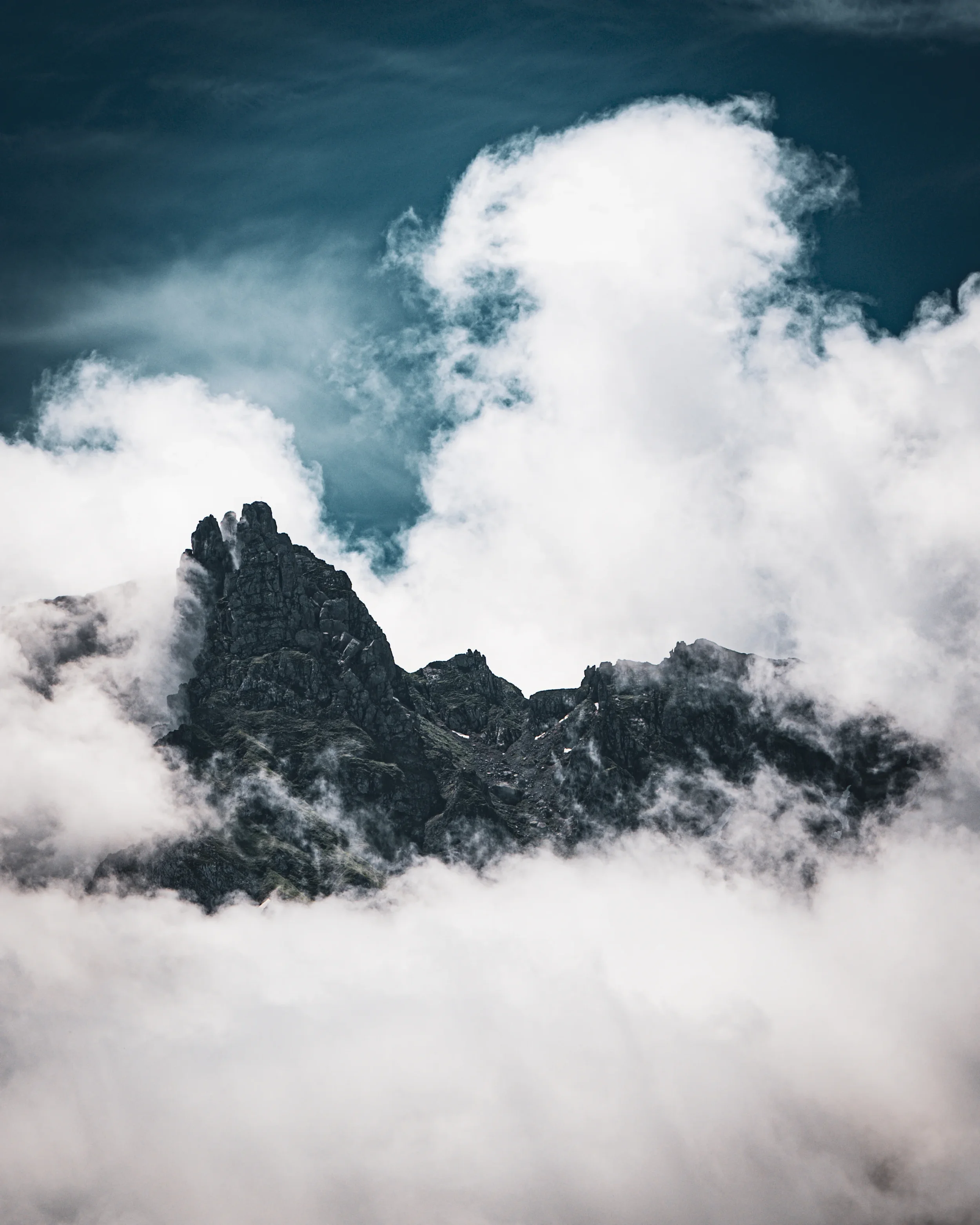 Montagne rocheuse émergeant de nuages avec un ciel nuageux en arrière-plan.