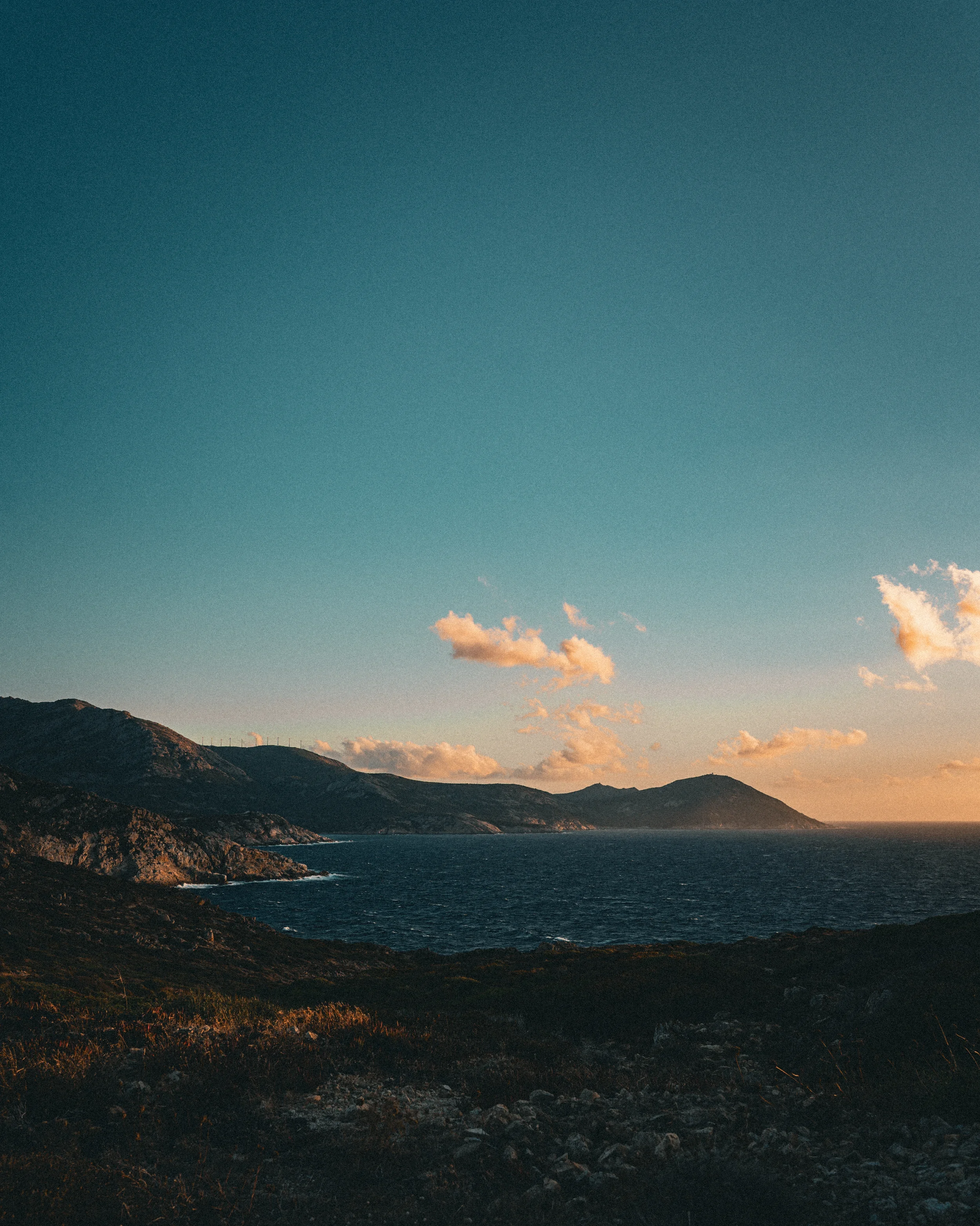 Coucher de soleil sur une côte rocheuse avec la mer, montagnes et ciel avec quelques nuages