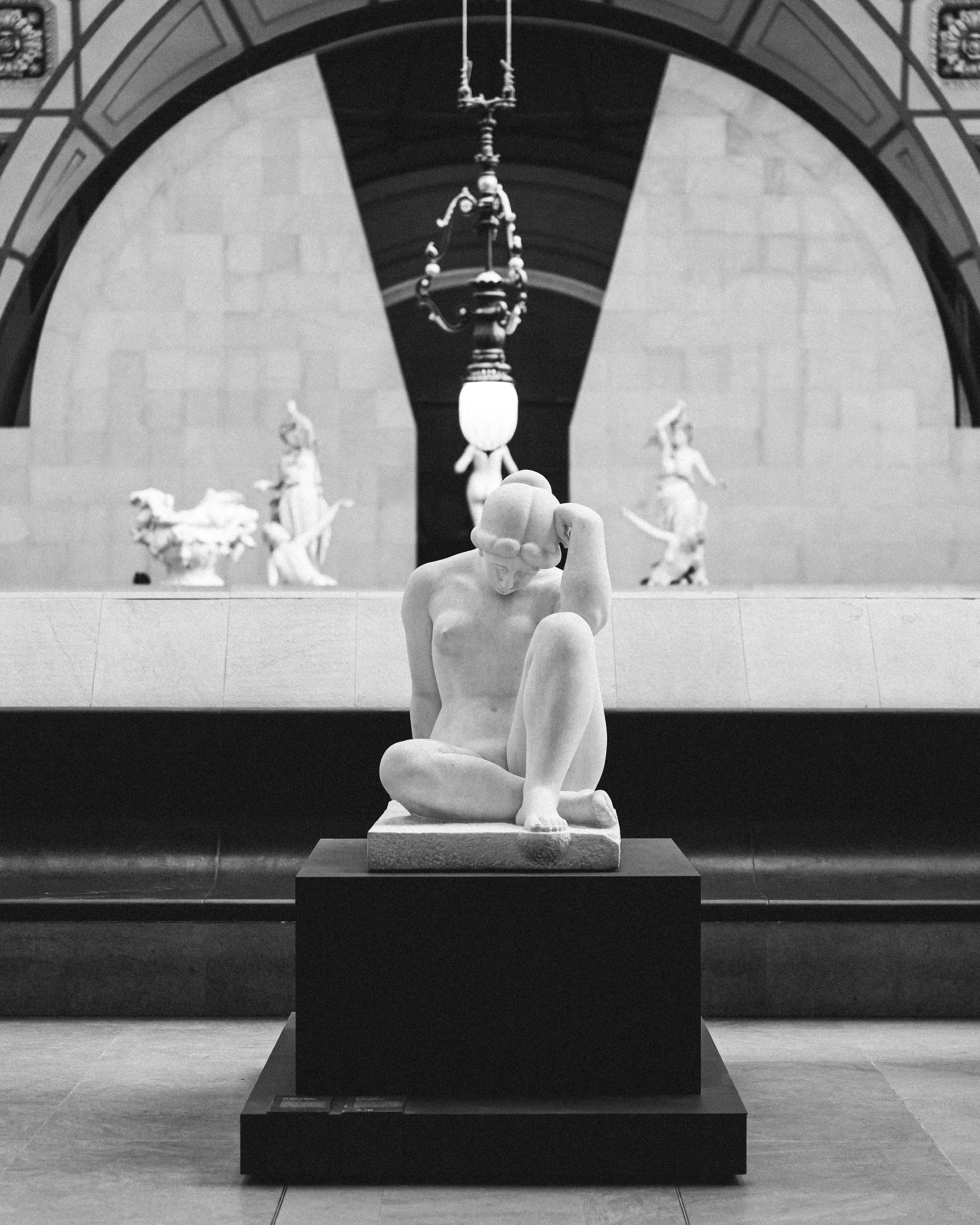 Sculpture en marbre d'une femme assise, tête penchée, dans un musée d'art classique.