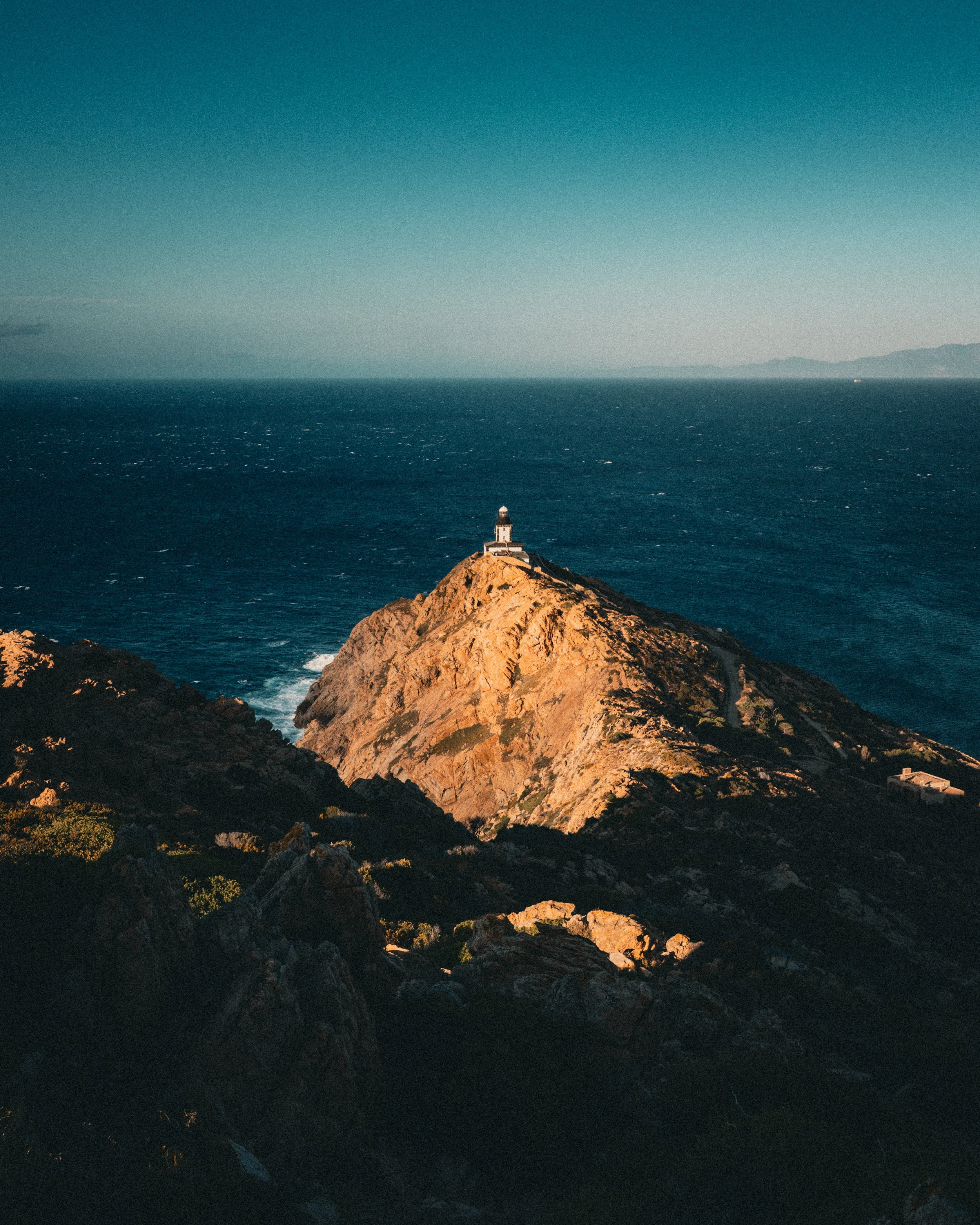 Phare situé sur une falaise rocheuse surplombant l'océan sous un ciel dégagé.