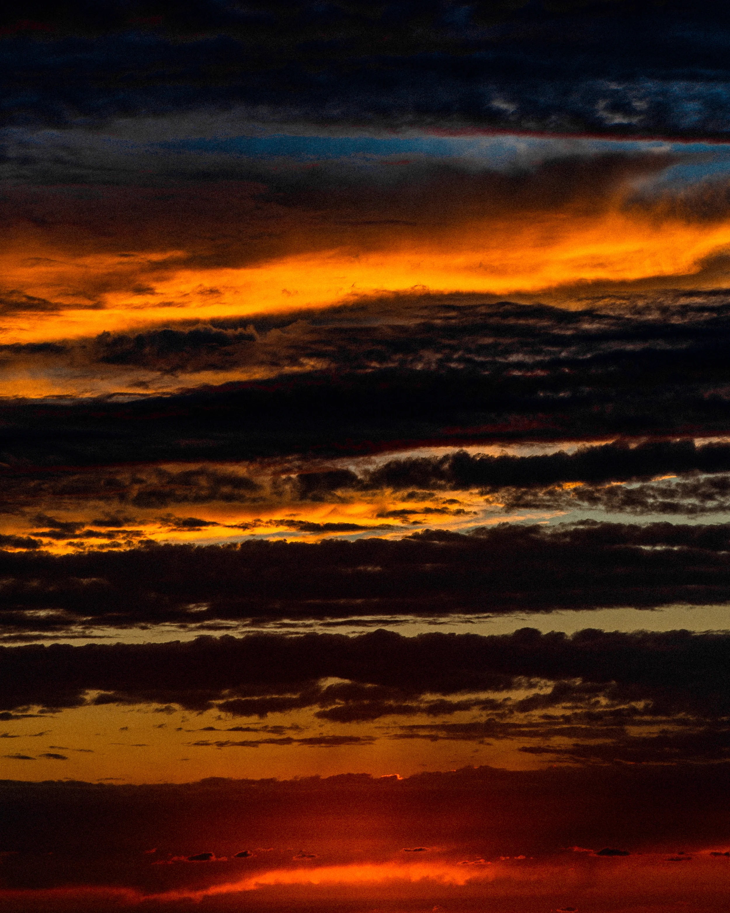 Coucher de soleil avec des nuages sombres et des teintes orange, rouge et jaune dans le ciel.
