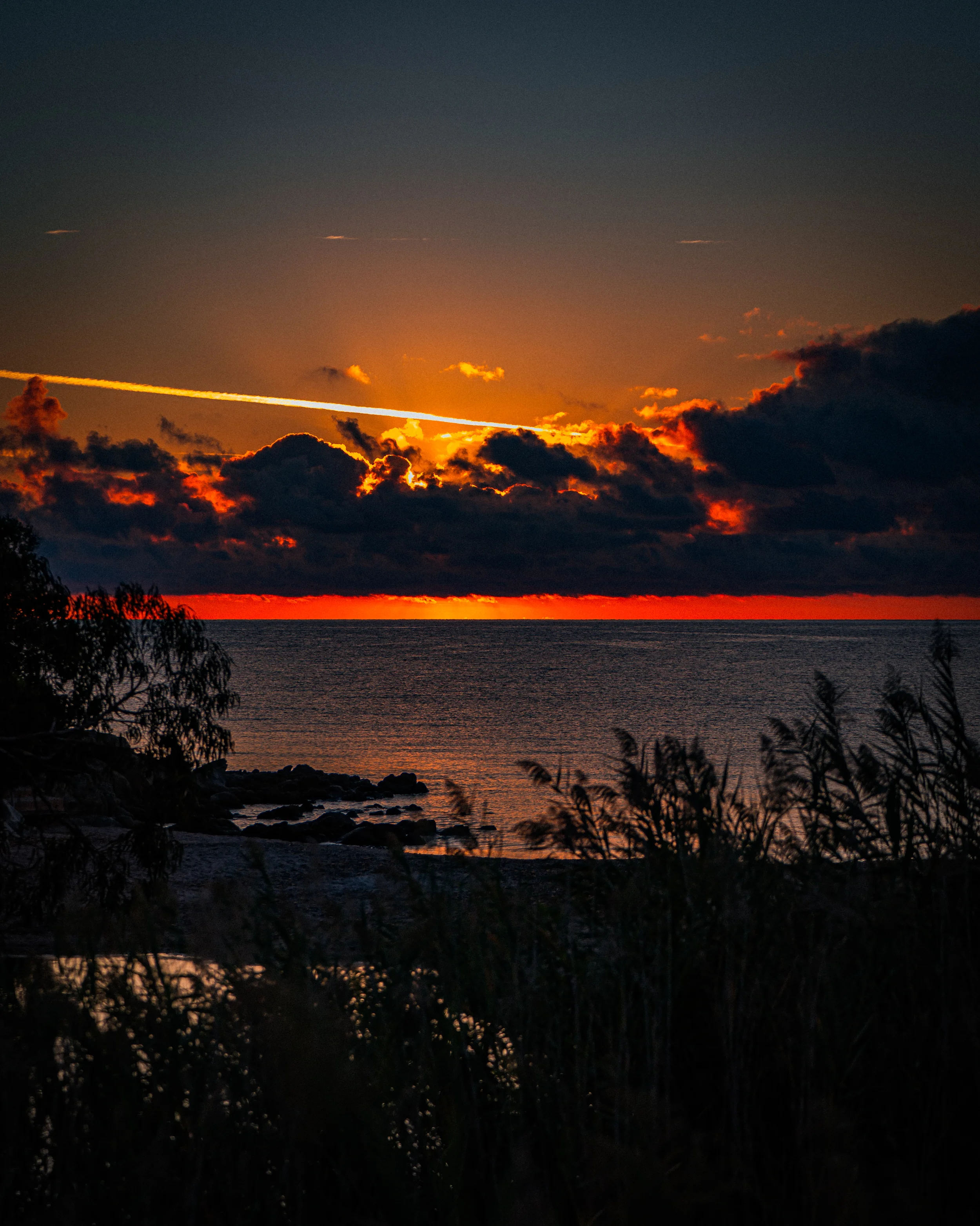 Coucher de soleil sur la mer avec des nuages sombres et un ciel orange.