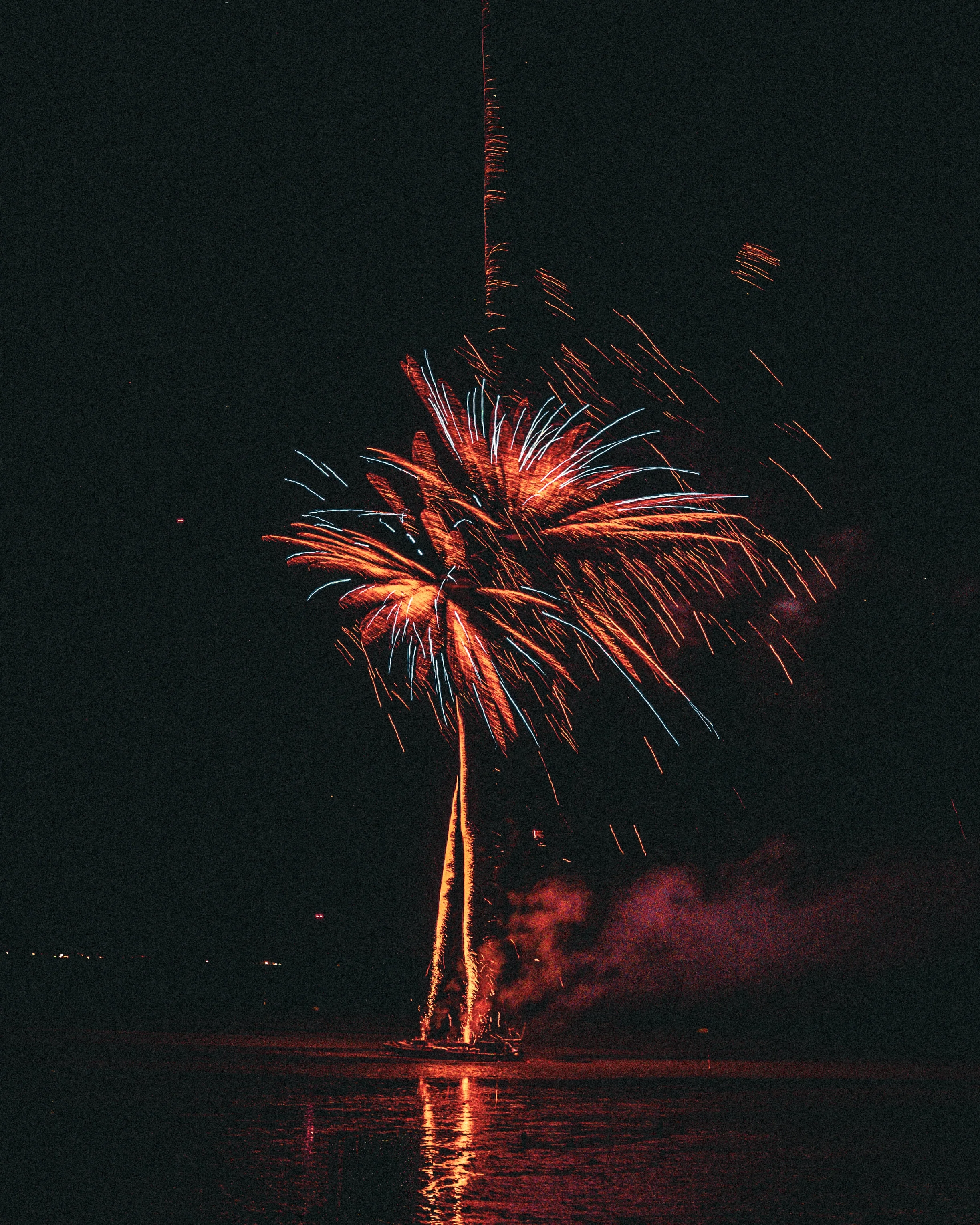 Feux d'artifice éclatant dans le ciel nocturne au-dessus de l'eau, avec reflet lumineux sur la surface de l'eau.