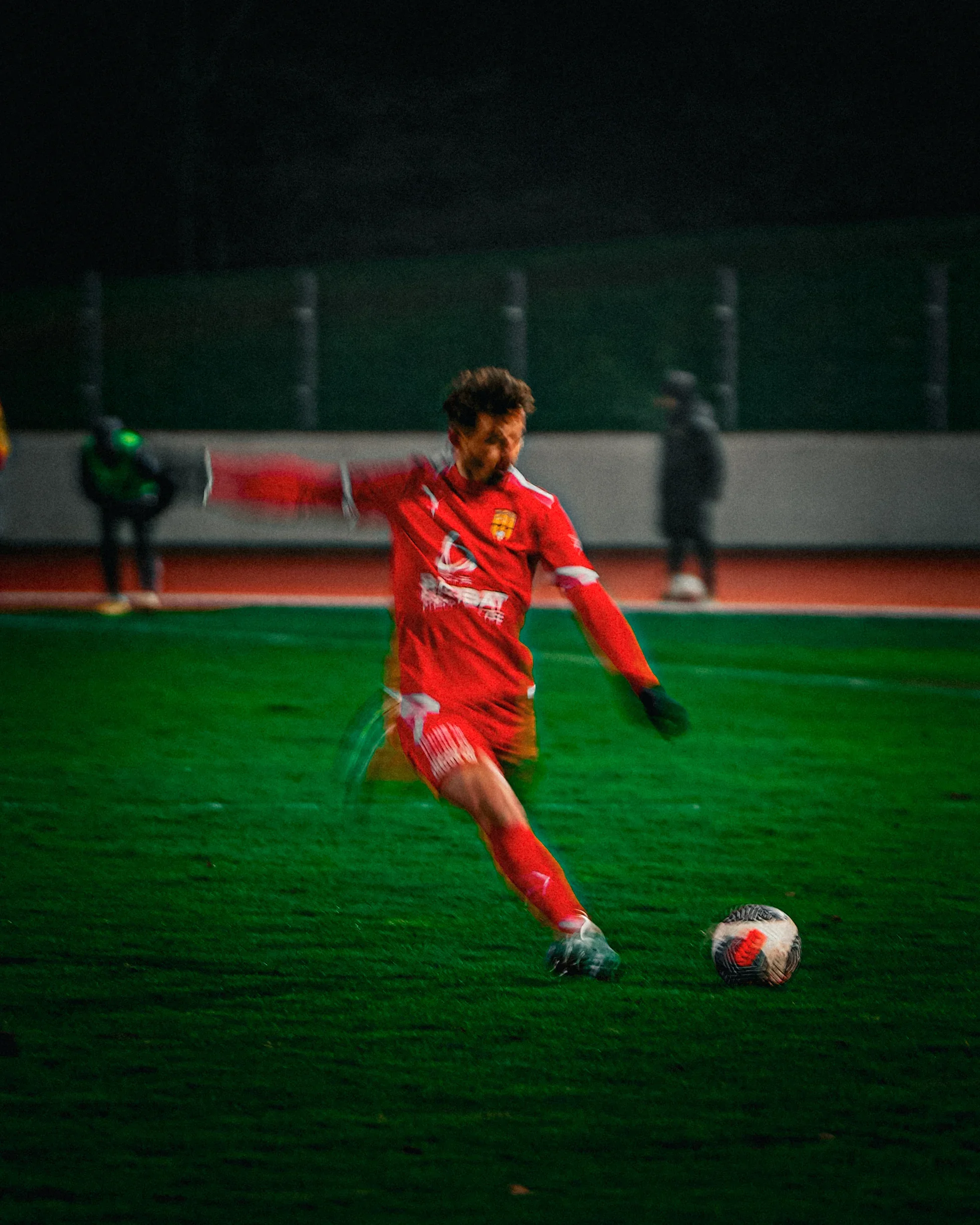 Un joueur de football en rouge effectue un tir au but lors d'un match nocturne.