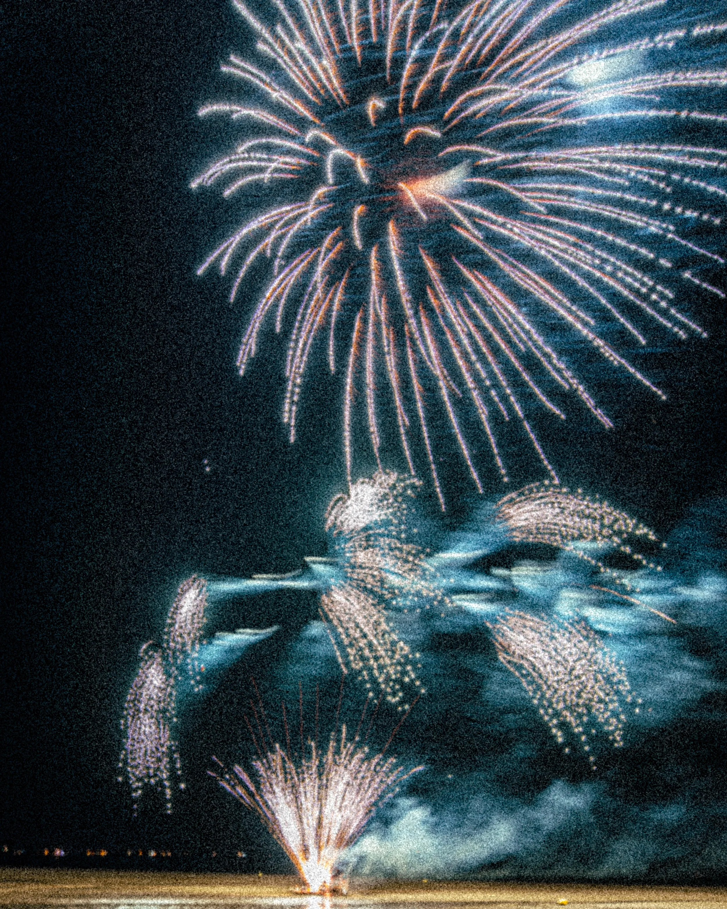 Feux d'artifice colorés illuminant le ciel la nuit au-dessus de l'eau, avec des reflets lumineux.