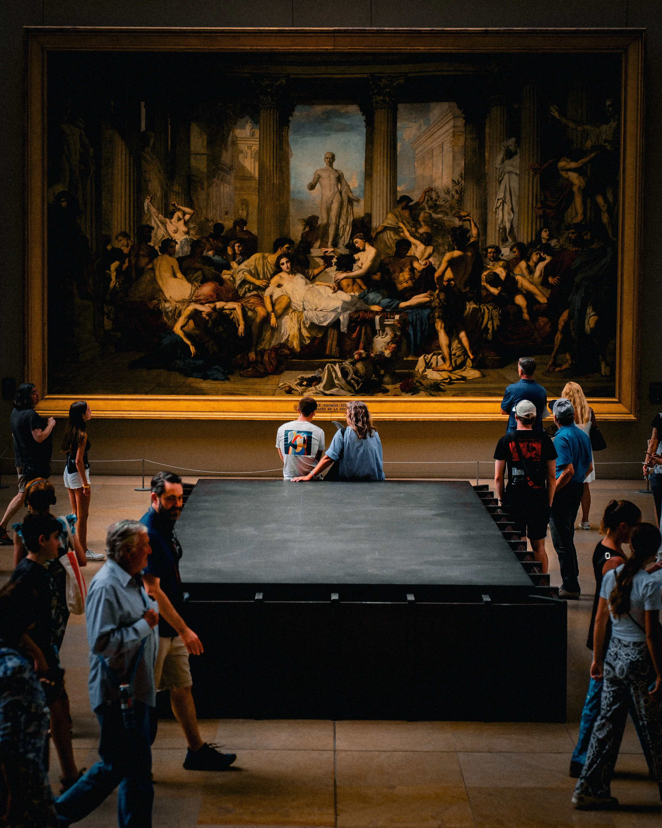 Groupe de visiteurs dans un musée regardant une grande peinture historique encadrée au mur.