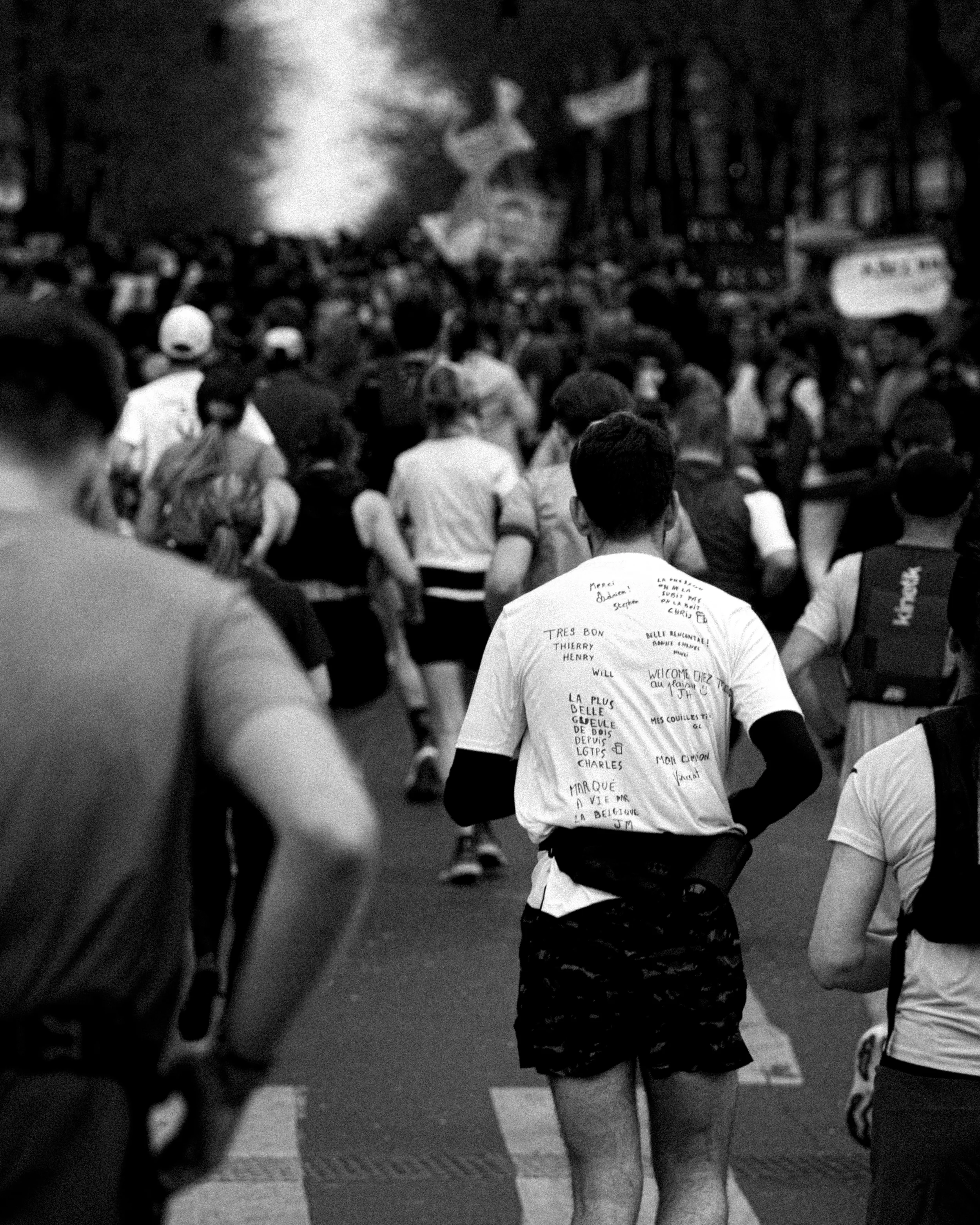 Une foule de personnes qui participent à une marche ou une manifestation dans une rue, avec des pancartes visibles au loin.