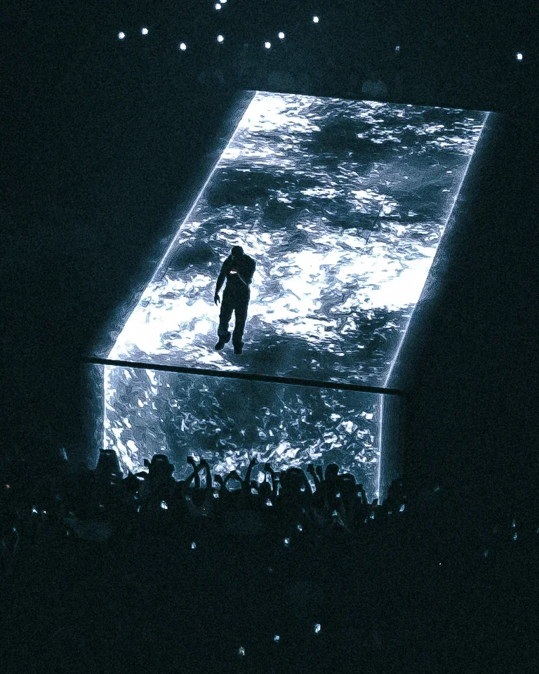Une personne flotte au-dessus d'une grande surface de projection d'eau ou de lumière, dans un environnement sombre avec un public takant des photos.