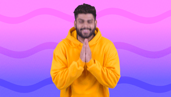 A young man with dark hair and a beard, wearing a yellow hoodie, is smiling with his hands pressed together in a prayer position against a colorful, wavy pastel background.