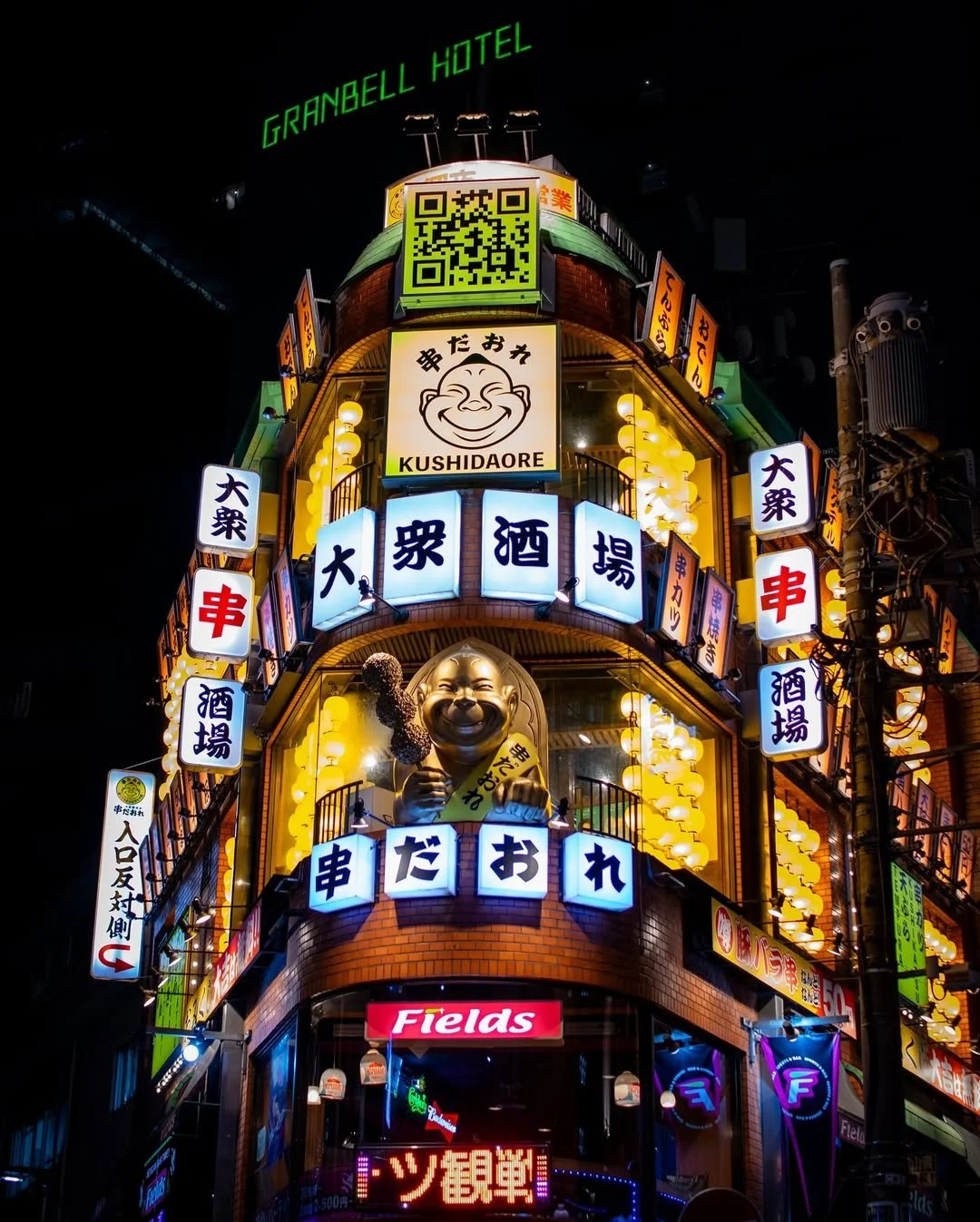 Brightly lit building at night in Japan with signs in Japanese, a smiling statue holding skewers, and a sign for Kushidaore.