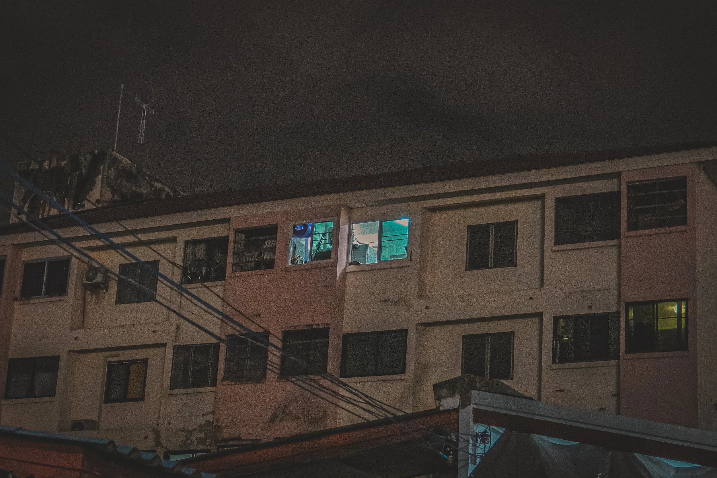 Nighttime view of an apartment building with lit windows and visible laundry drying outside on a balcony.
