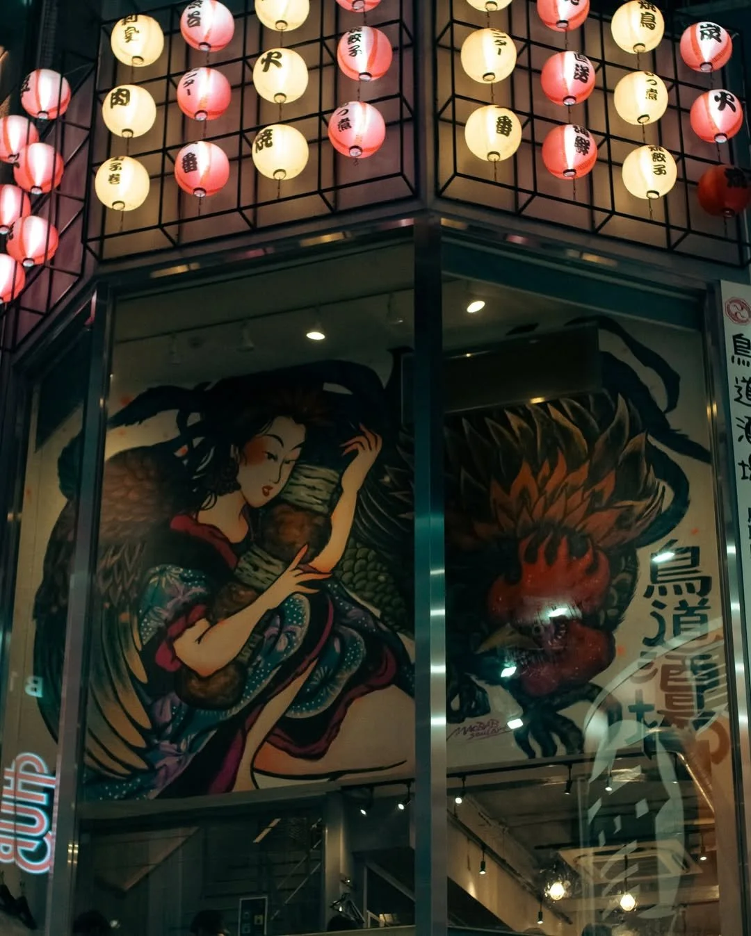 Traditional Japanese lanterns hanging on the exterior of a building, with a large illustrated poster of a woman holding a dragon in a colorful, stylized Japanese art style.