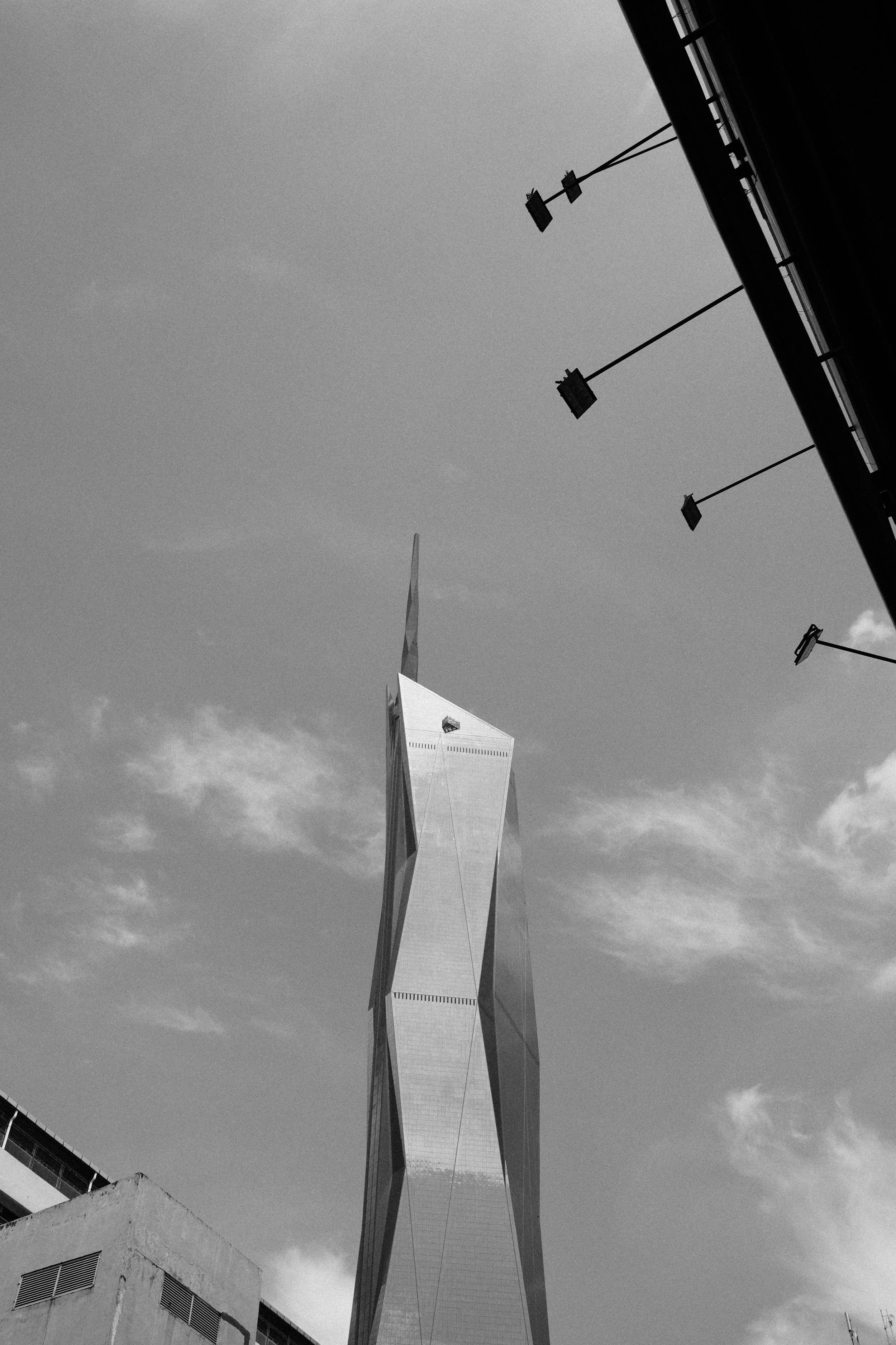 Black and white photo of a tall, modern skyscraper with sharp, angular design, taken from below with a partly cloudy sky background.