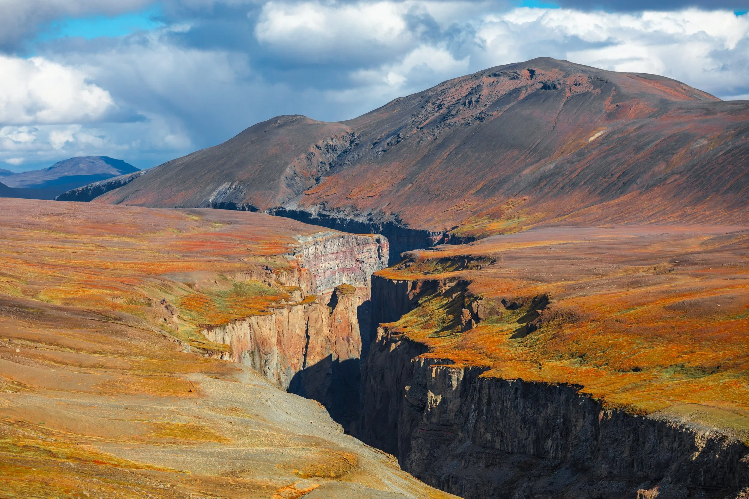 Dramatic volcanic mountain landscape with deep basalt canyon, red tundra, and storm clouds