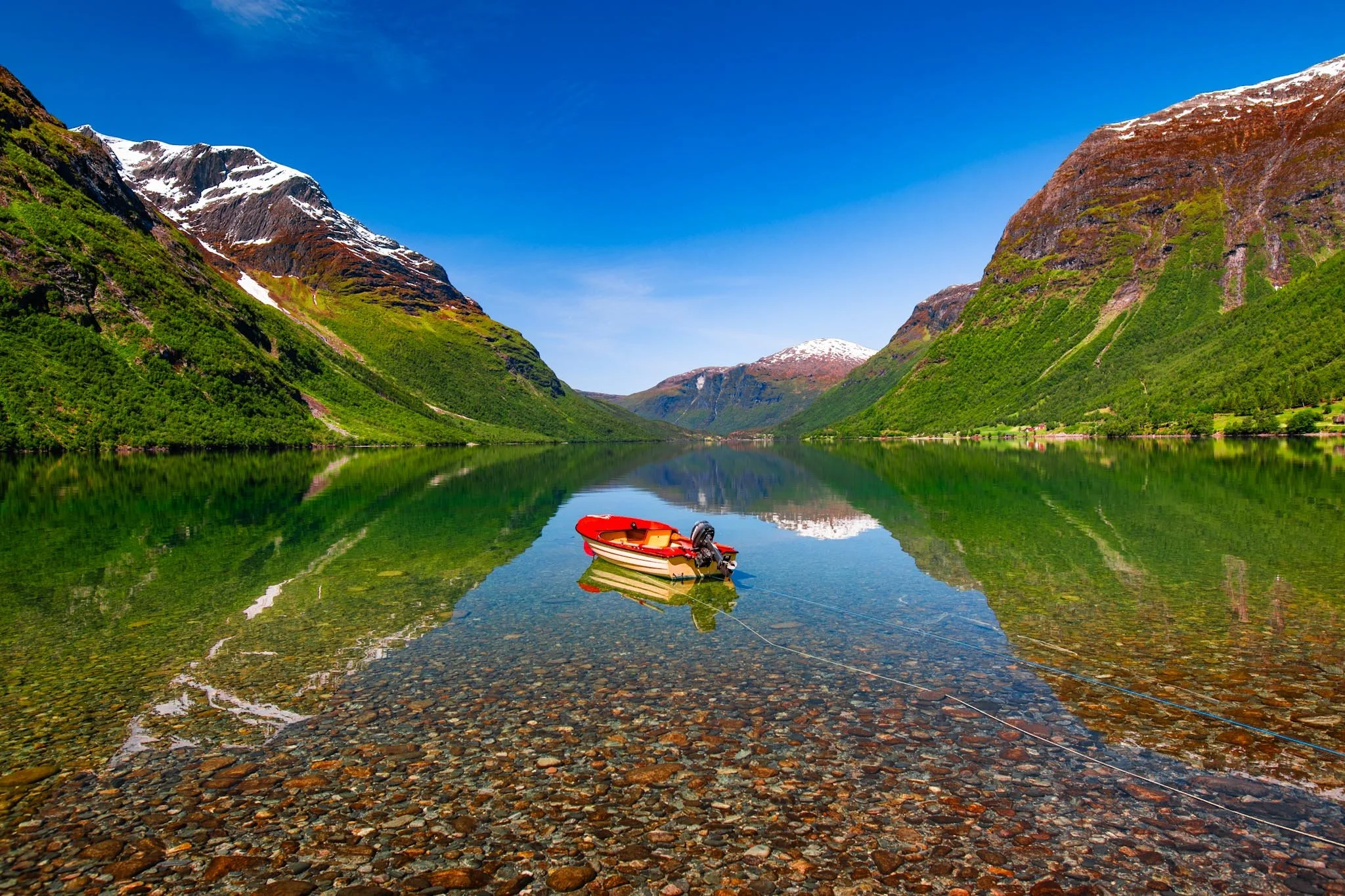 Small boat on a calm fjord in Norway with clear reflection of mountains under bright even summer light