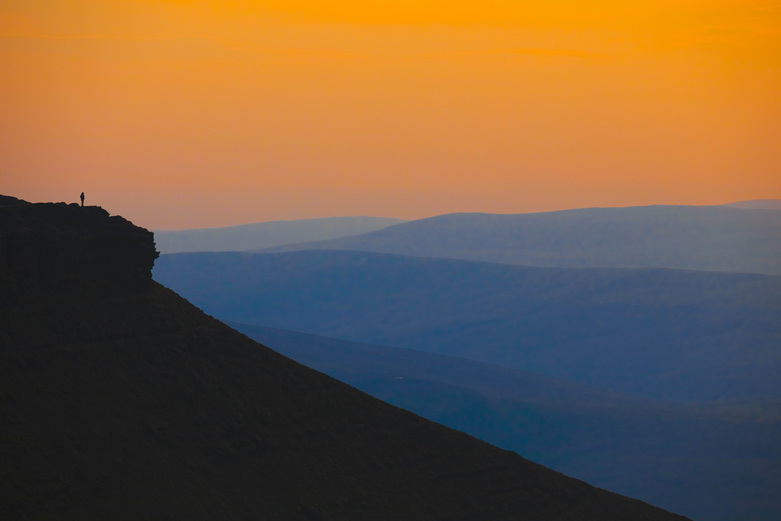 Warm orange sky above cool blue mountain layers in Wales showing natural colour temperature contrast in a landscape