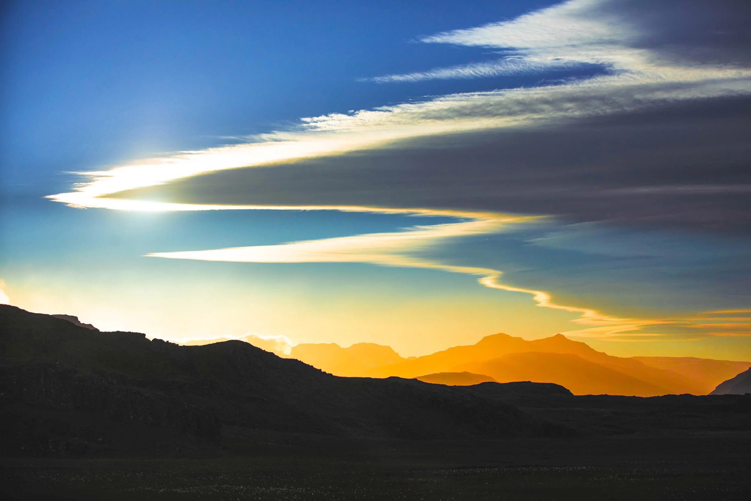 Dramatic sunset over silhouetted mountain ranges beneath sweeping clouds