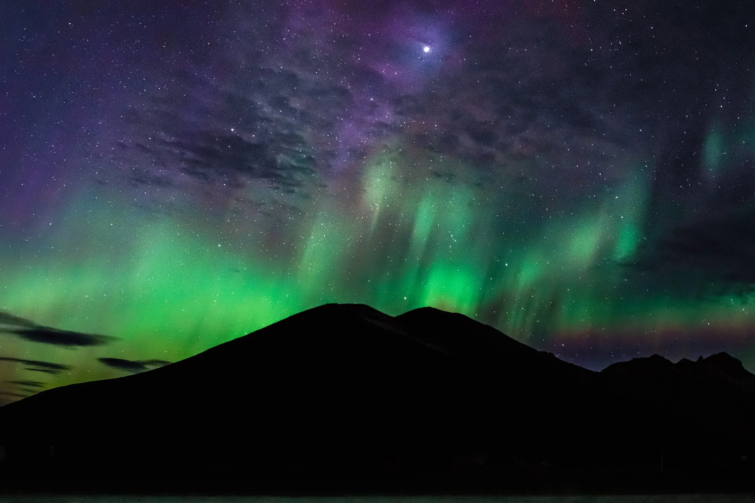 Green and purple Northern Lights over a silhouetted mountain range beneath a star-filled night sky