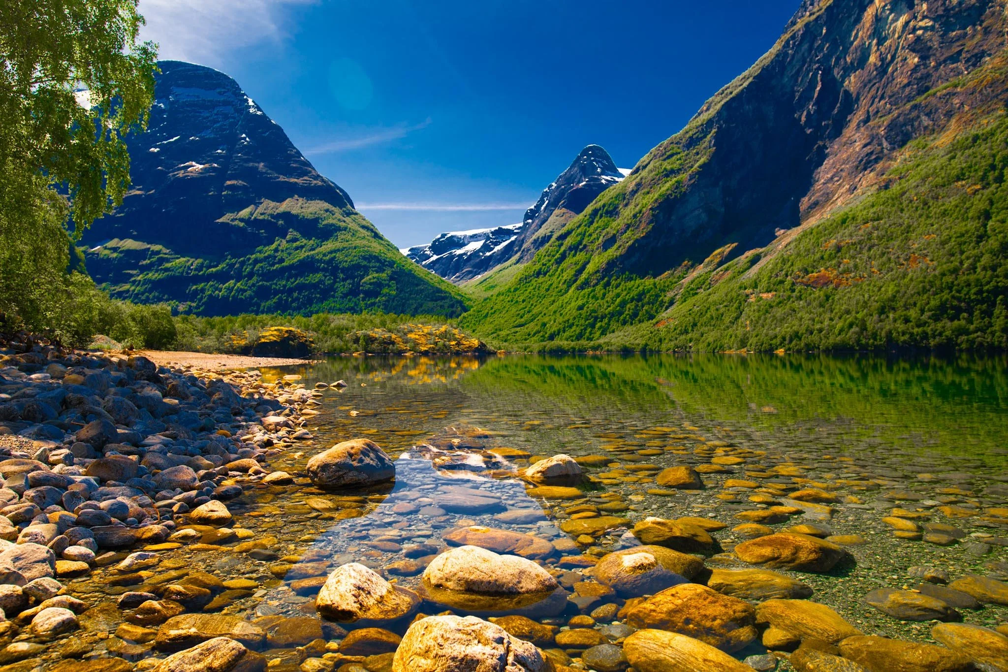 Clear lake in Norway with rocky foreground and mountains under bright summer light