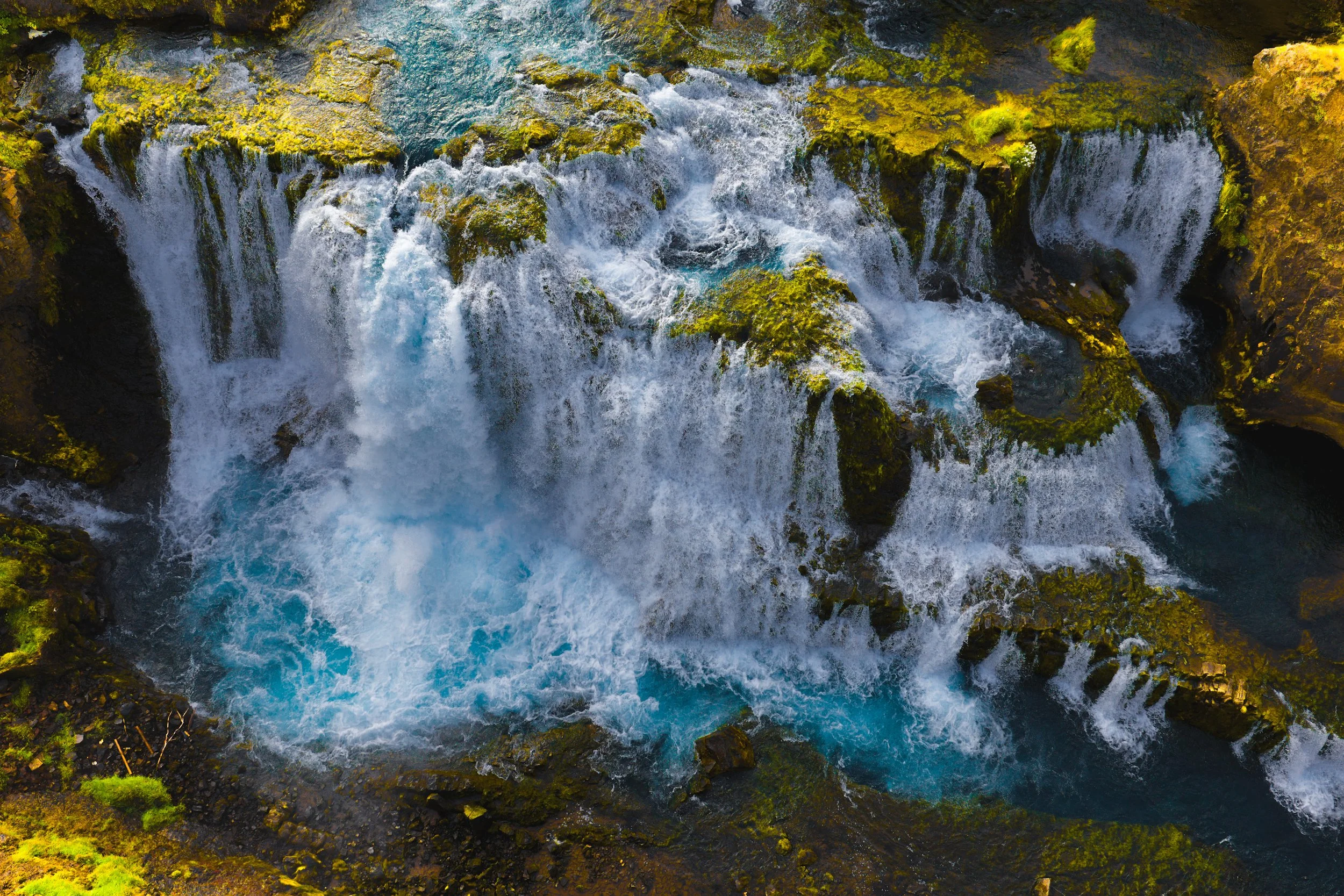 Turquoise waterfall rushing over moss-covered volcanic rocks