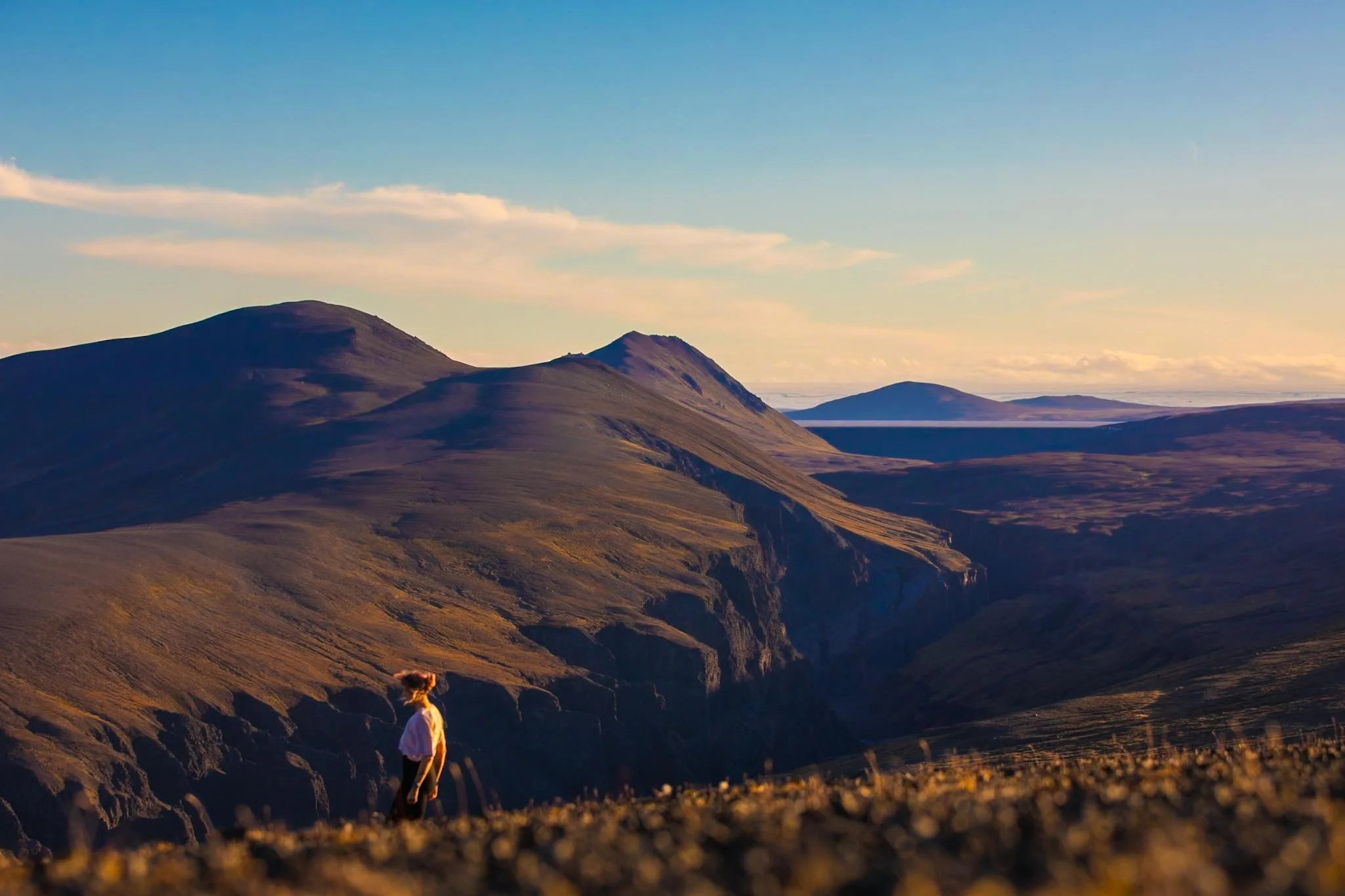 Woman standing on mountain ridge at golden hour overlooking deep valley and distant peaks