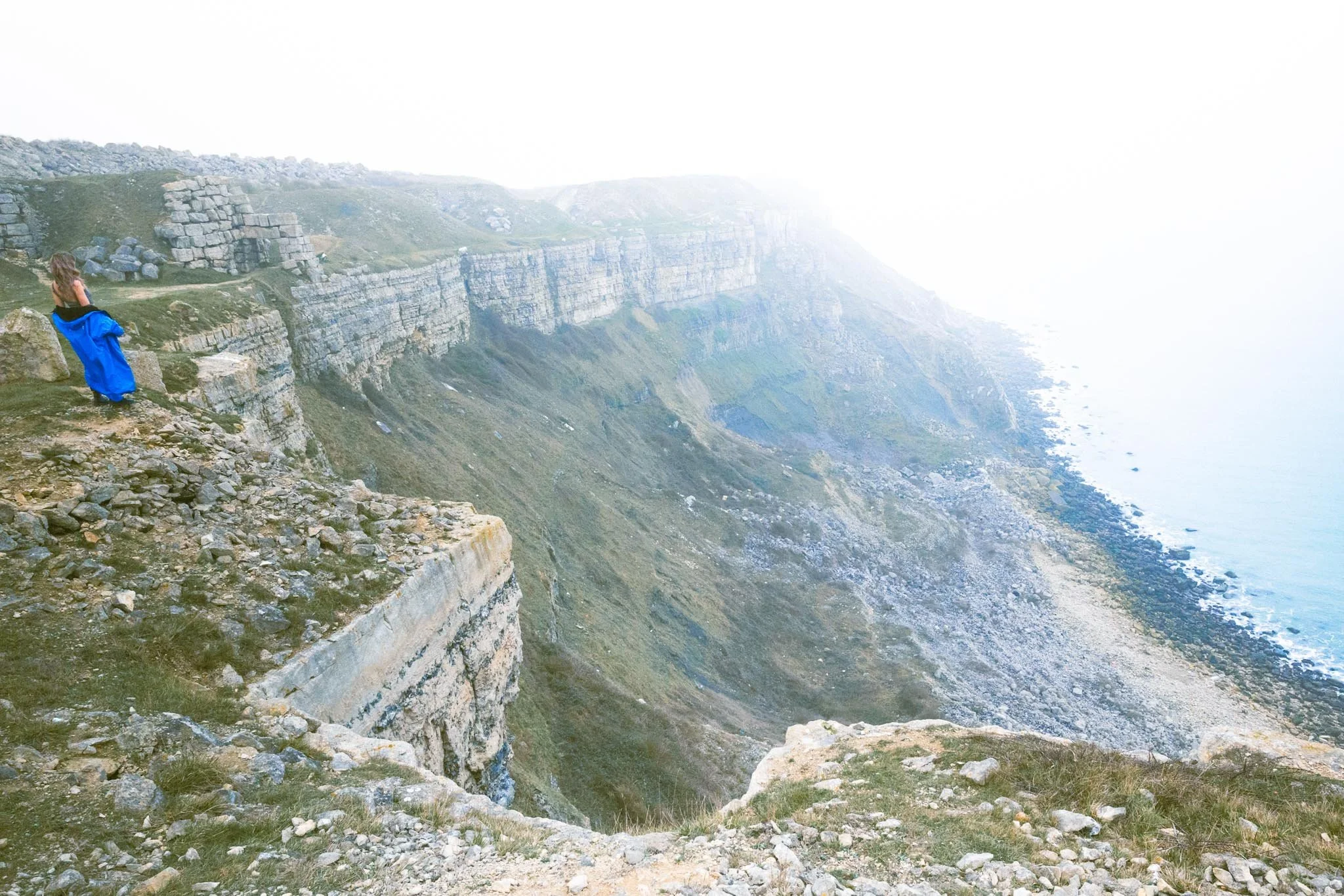 Woman standing on cliff edge overlooking misty coastline and steep rocky cliffs