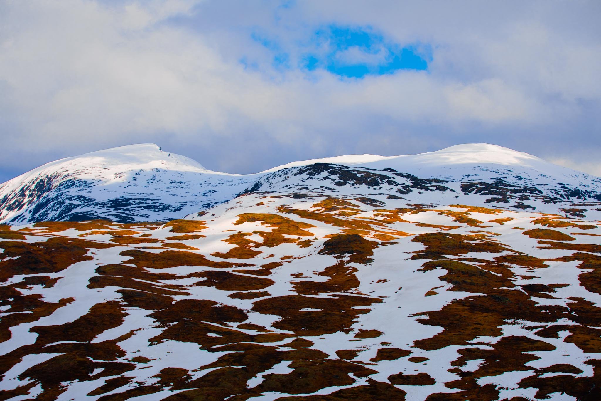 Snowy mountain peaks in Norway with brief light breaking through clouds