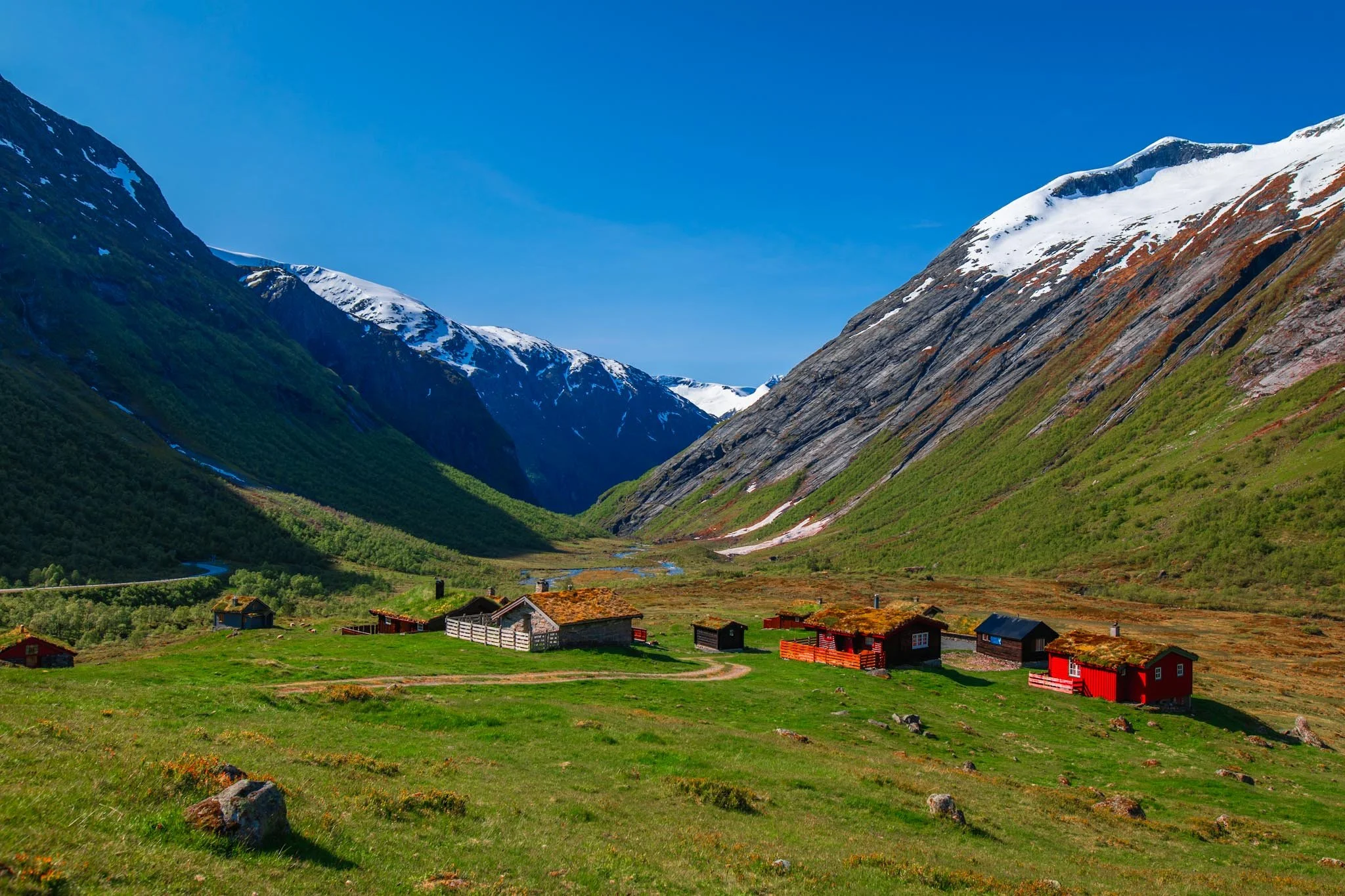 Green valley with cabins in south-west Norway surrounded by snow-covered mountains under bright summer light