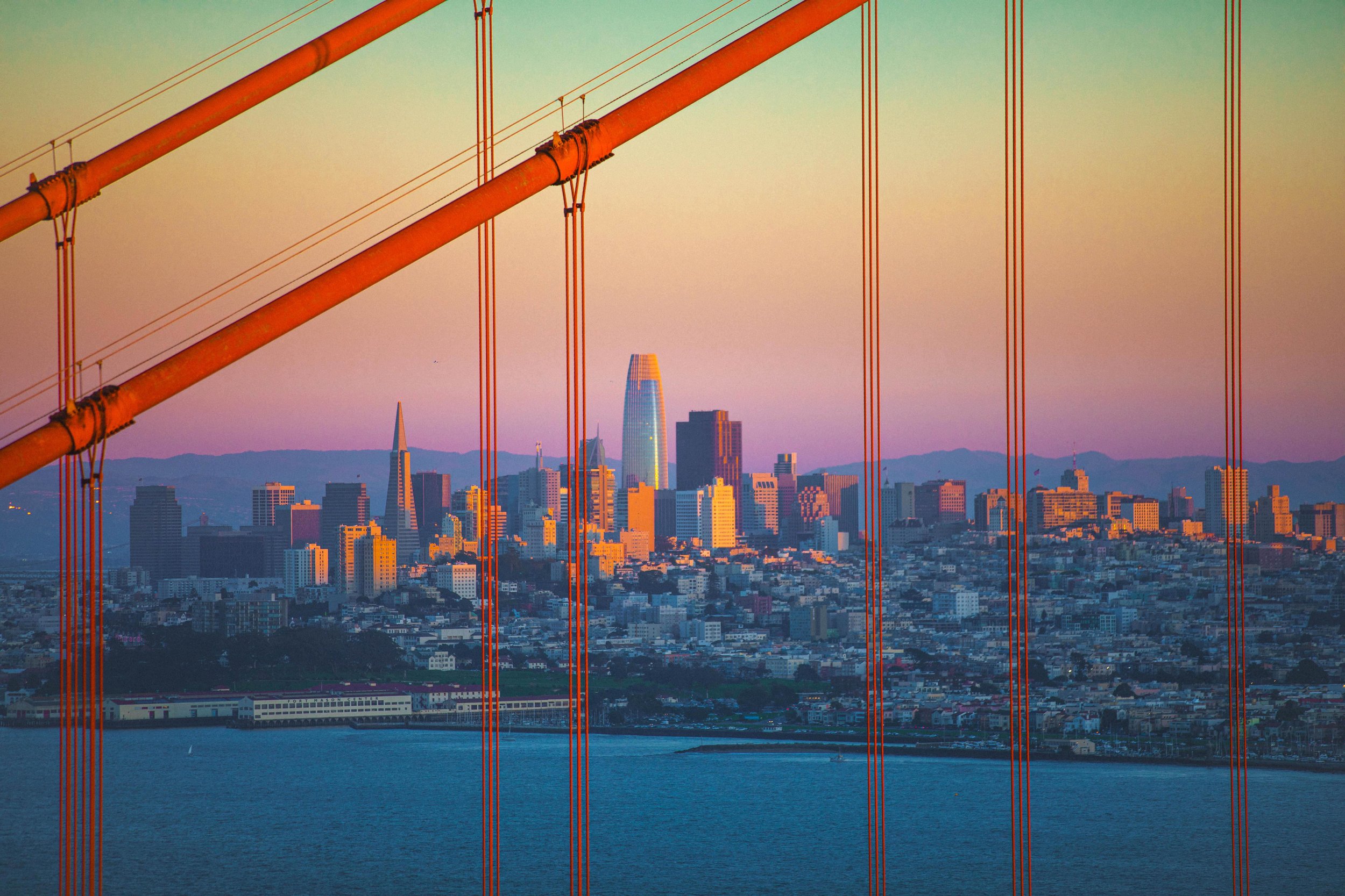 Golden Gate Bridge cables framing San Francisco skyline at sunset with strong warm and cool colour contrast