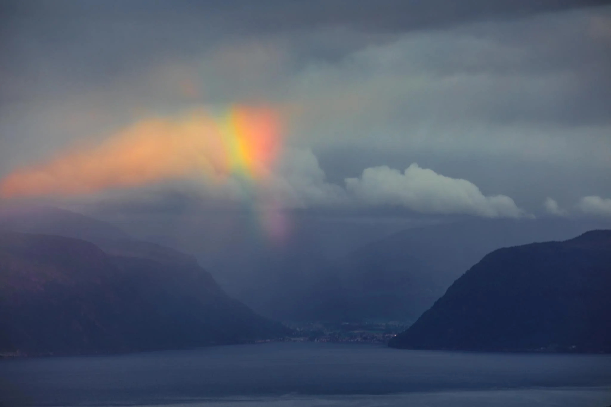Rainbow over a fjord in Norway with dark clouds creating strong contrast