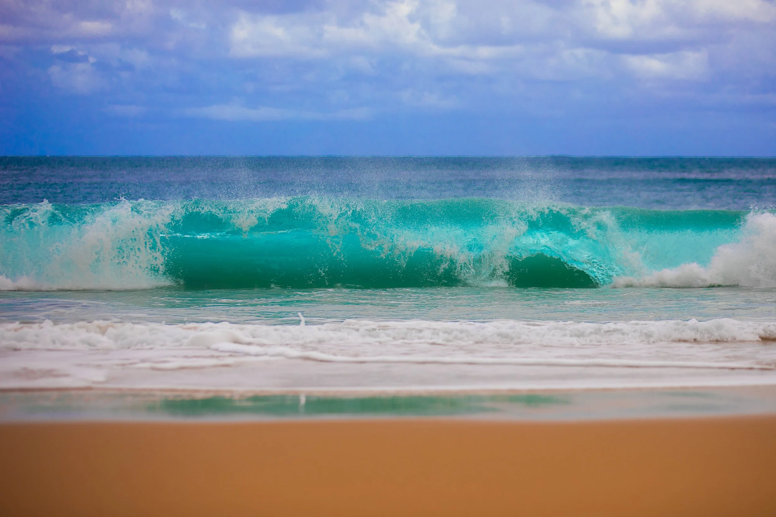 Turquoise ocean wave breaking on a sandy beach showing natural colour contrast between water, sand and sky