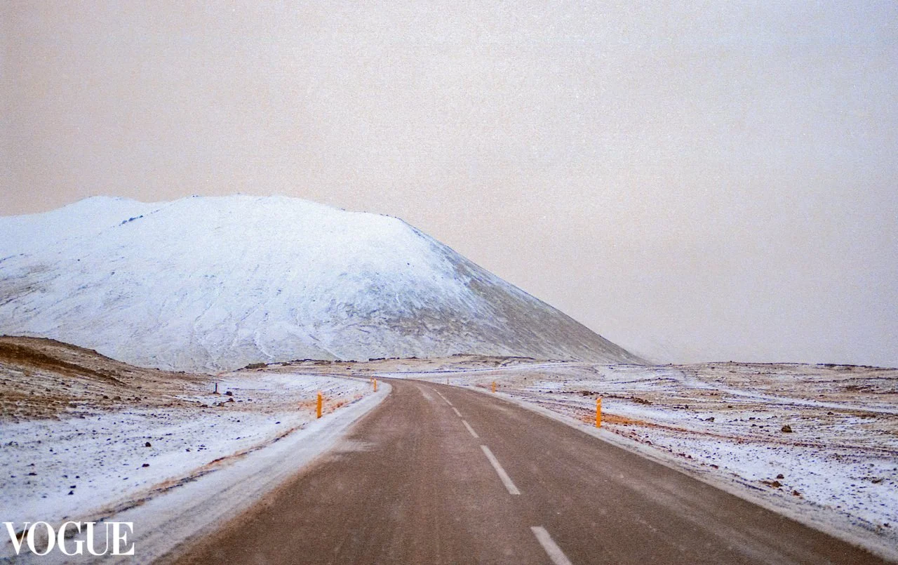 Snow-covered mountain beside an empty two-lane road in an Icelandic landscape