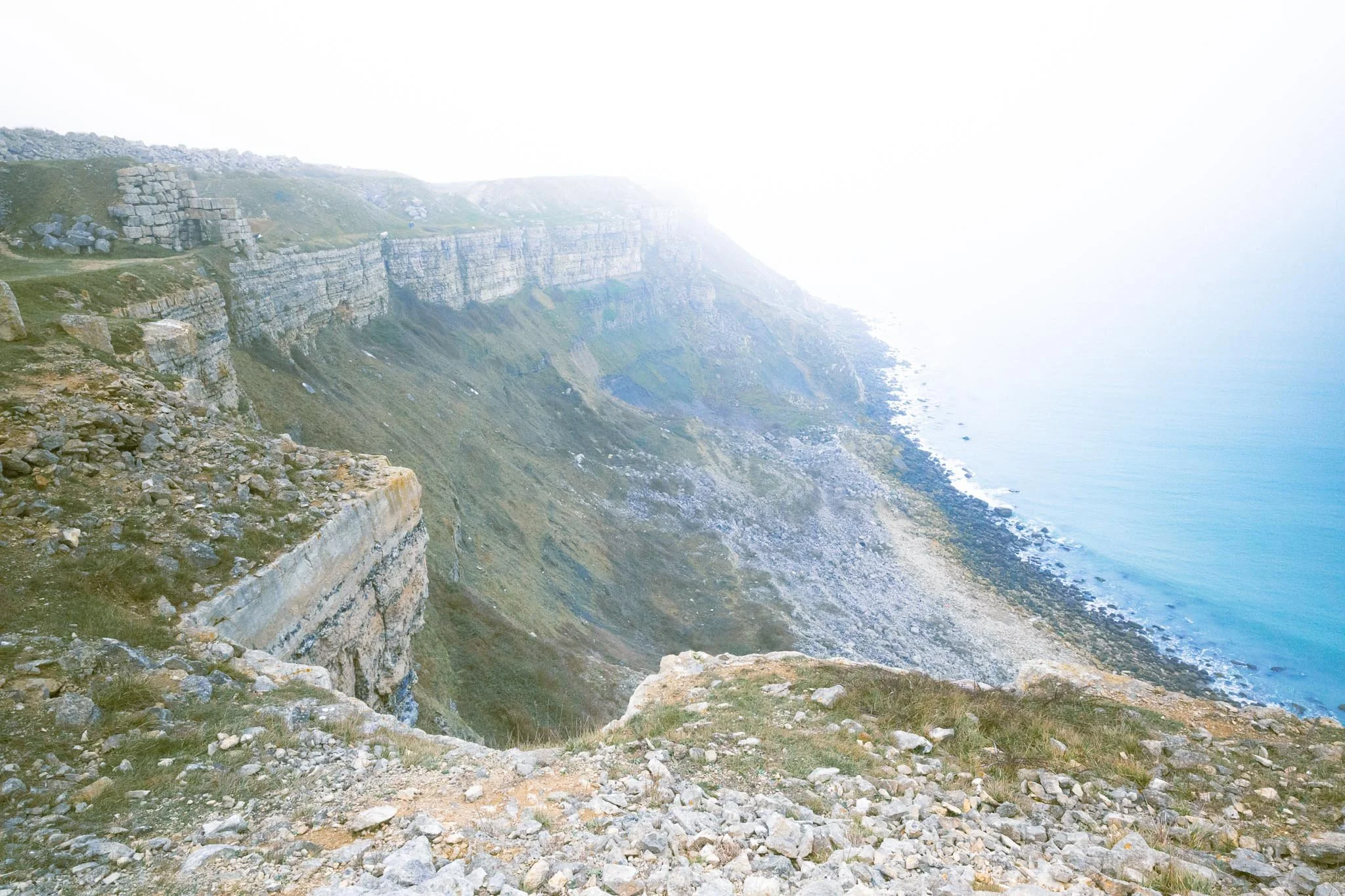 Misty coastal cliffs and rocky shoreline fading into soft light and sea