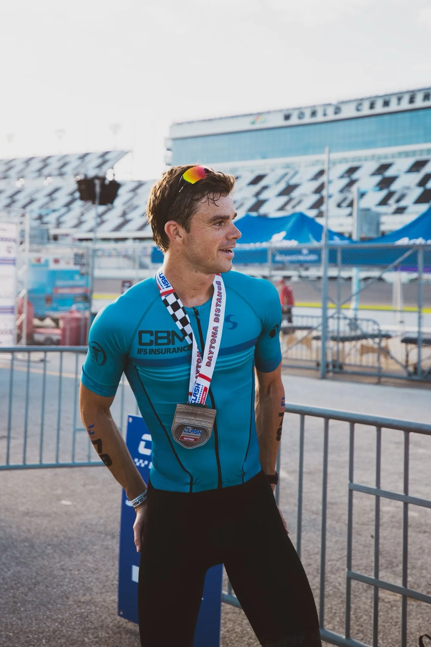 Triathlete wearing a blue cycling jersey with a medal around his neck, smiling after finishing a race at the World Center in Daytona.