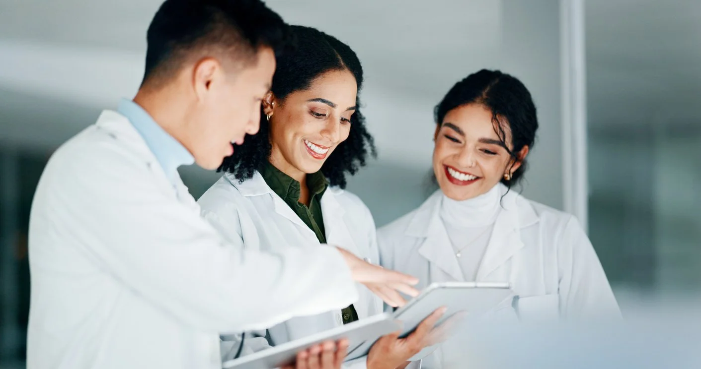 Three diverse scientists in lab coats looking at a tablet and smiling.