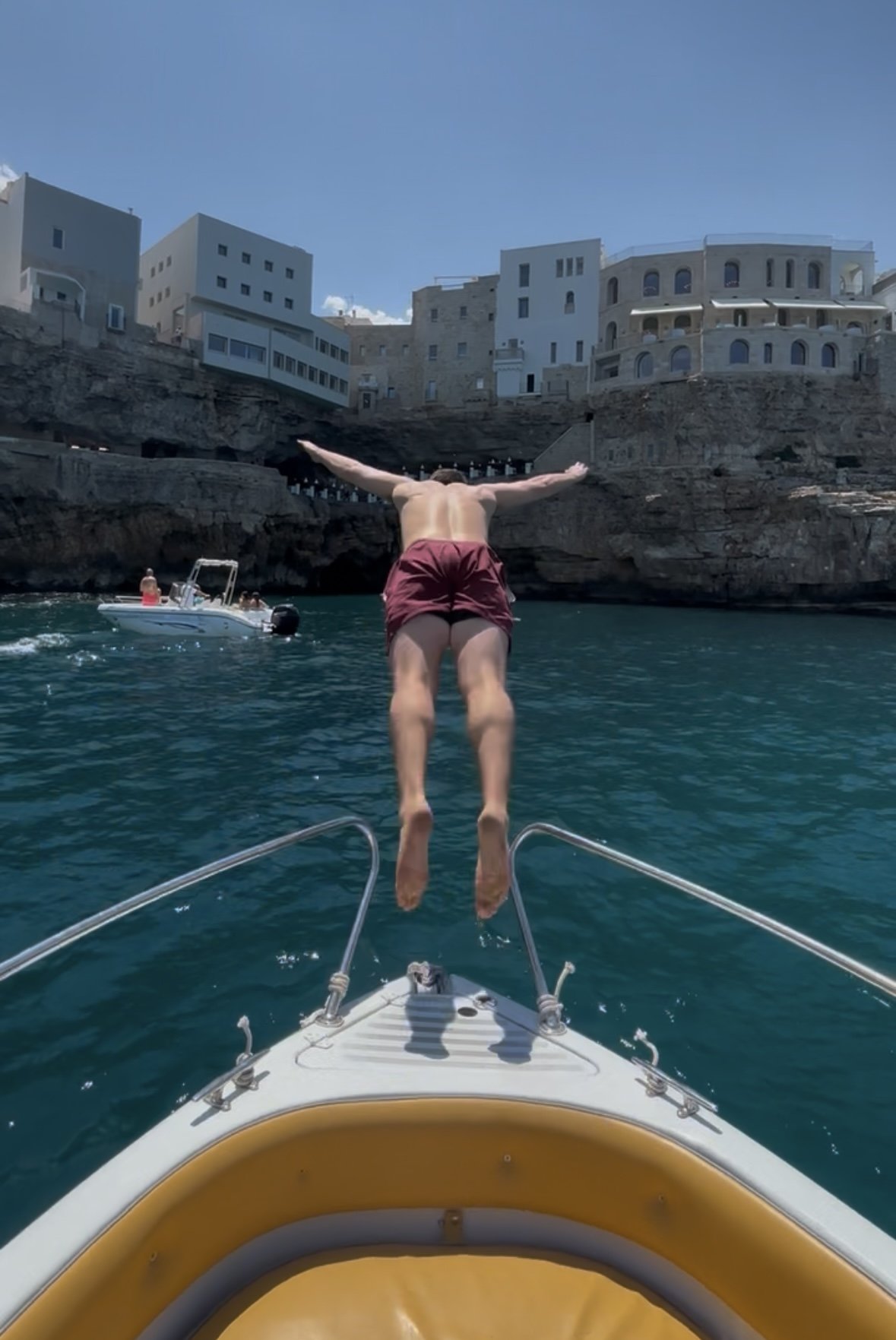 A man jumping into the water from a boat with some buildings in the background.