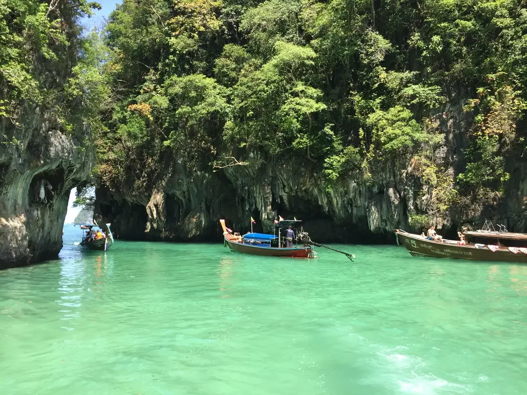 Boats floating in turquoise water near green, rocky cliffs covered with trees.