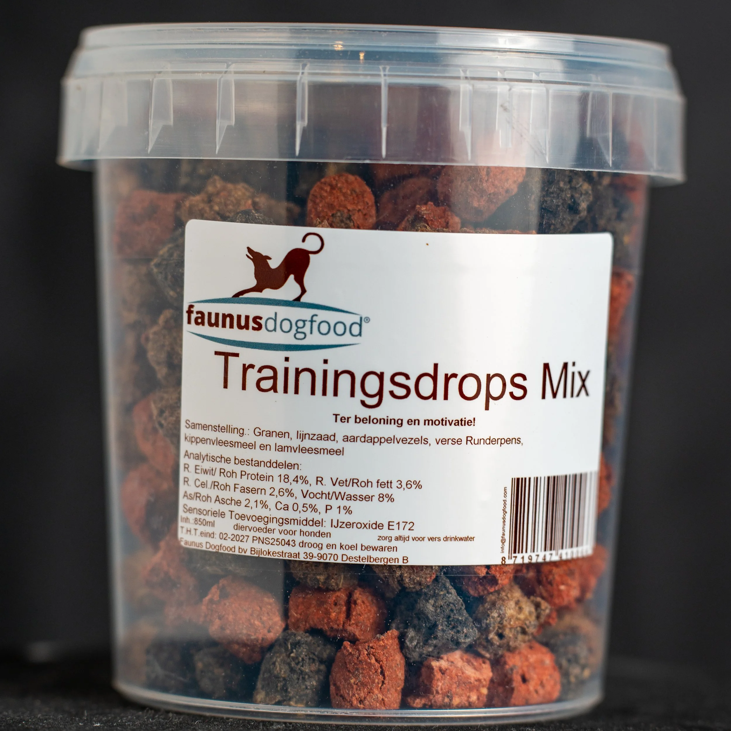 A clear plastic jar labeled 'Trainingdrops Mix' containing small, irregularly shaped dog training treats in various shades of brown and red, with a white label featuring a dog silhouette and text in Dutch and English.