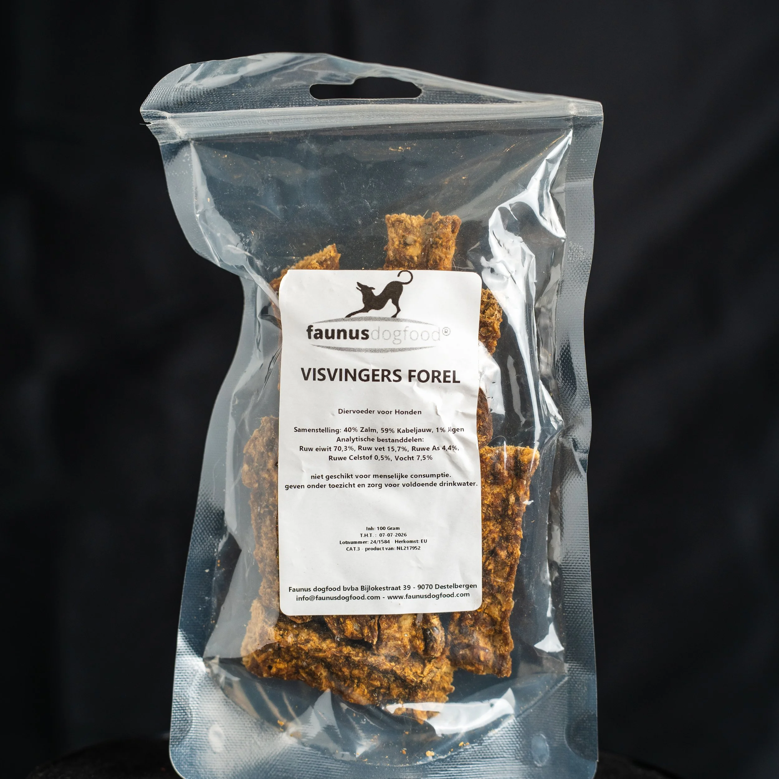 Clear plastic bag of dog treats labeled 'VISVINGERS FOREL' with a dog silhouette logo and Dutch text, set against a black background.