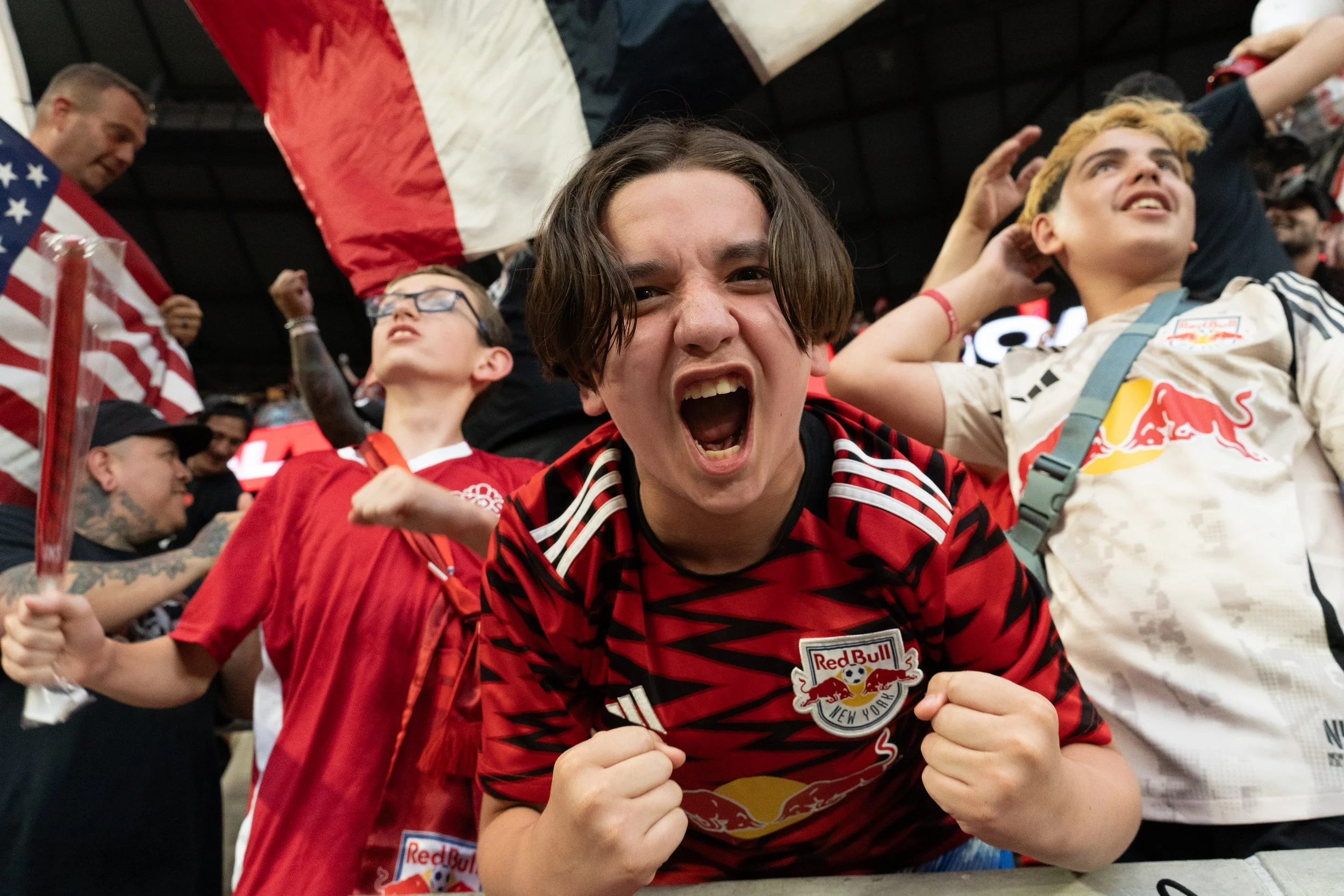 Group of passionate sports fans at a stadium, with some wearing Red Bull Racing jerseys, celebrating enthusiastically.