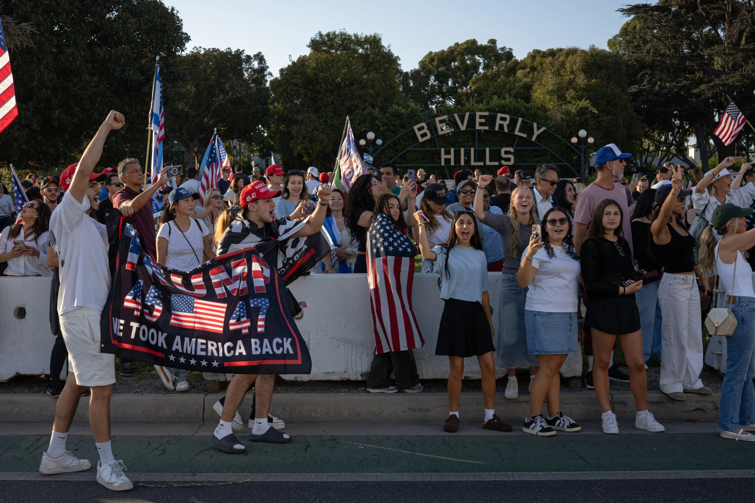 A large group of people gathered outdoors, many holding American flags and wearing patriotic clothing, participating in a patriotic rally or demonstration in Beverly Hills.