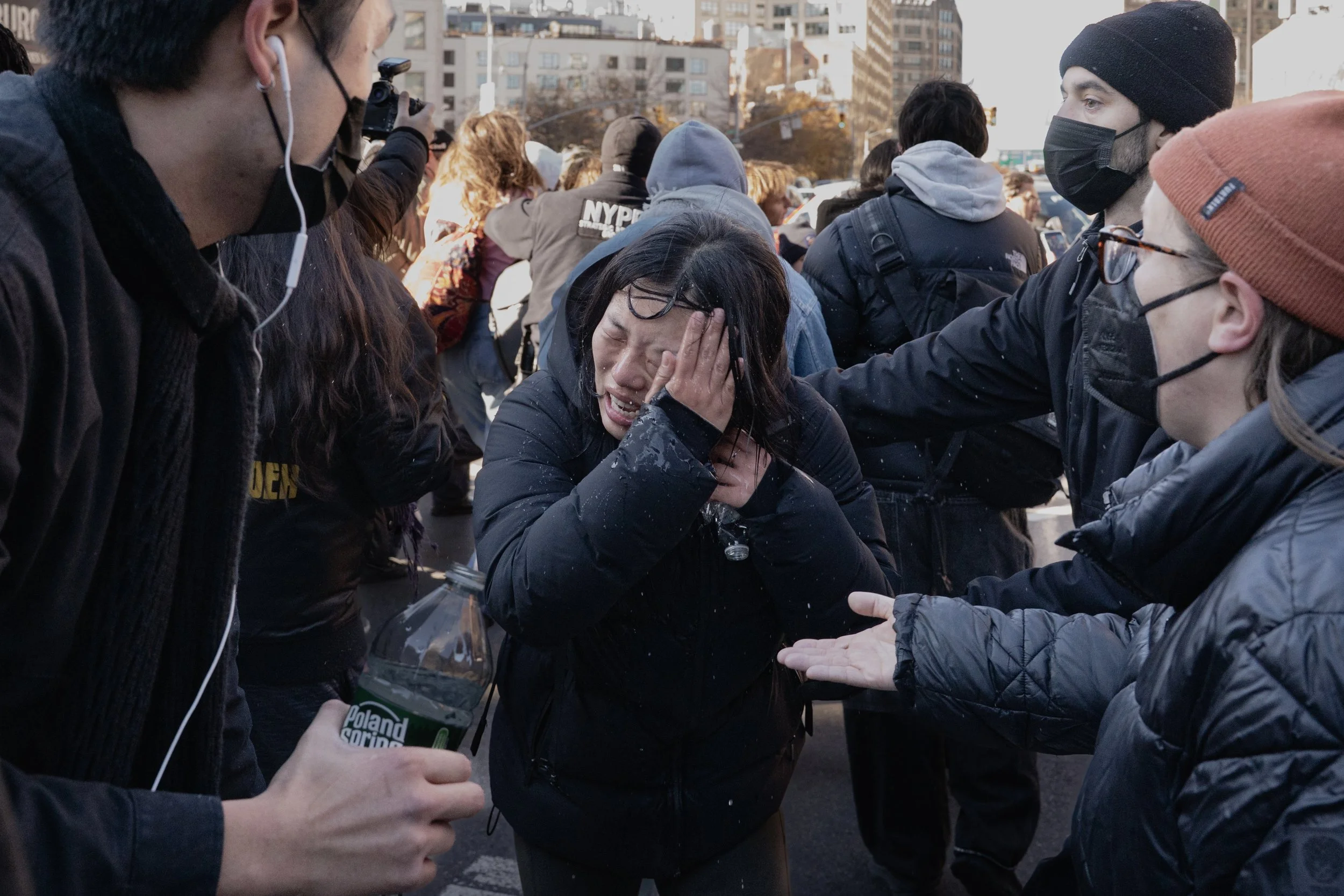 A woman appears to be crying and distressed as she is comforted by several people during a protest or demonstration on a city street, with others and city buildings in the background.