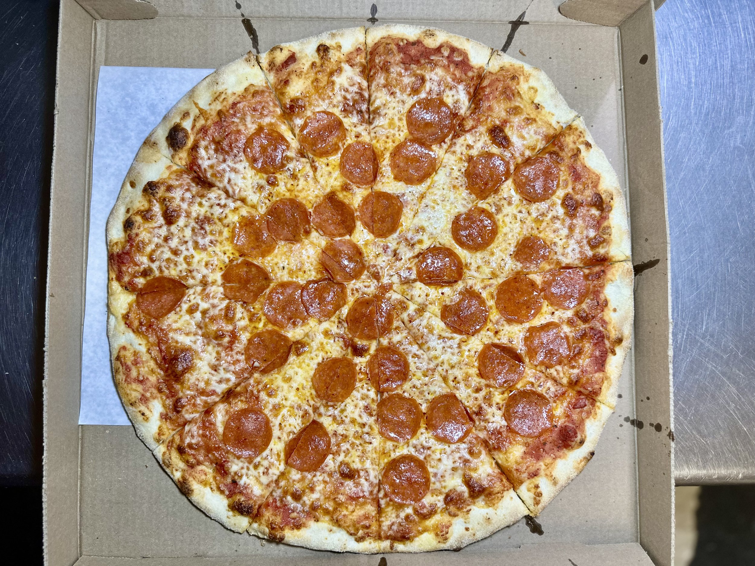 Pepperoni pizza in a cardboard box with cheese and pepperoni slices.