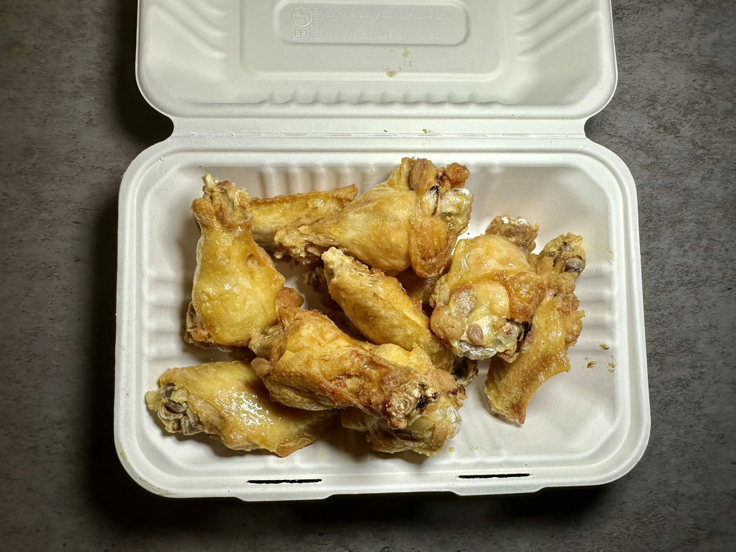 Six fried chicken drumsticks in a white foam takeout container on a gray surface.