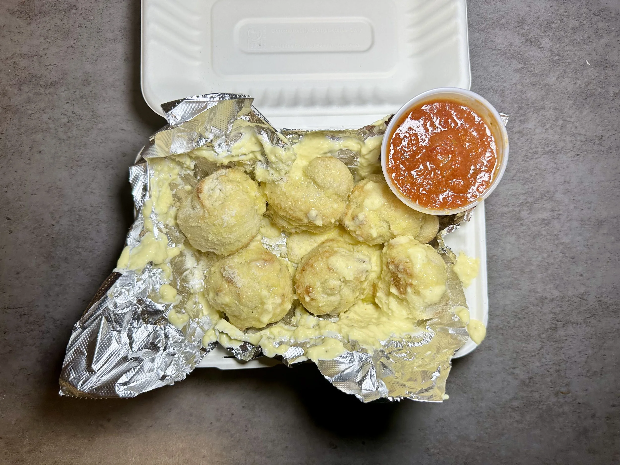 Fried cheese balls with yellow cheese sauce and a side of red sauce in a small container on a foam food tray.