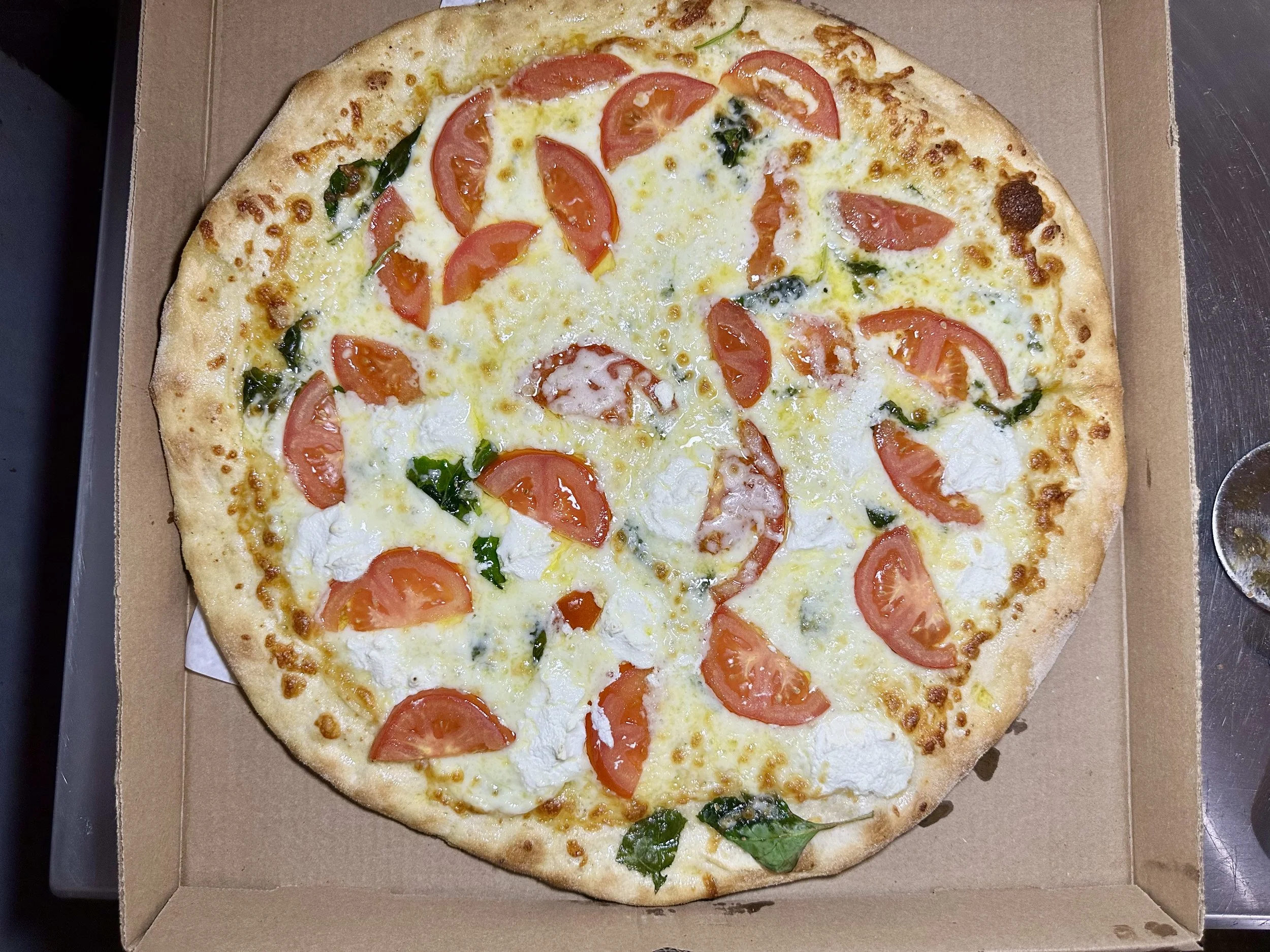 A vegetable pizza with tomato slices, fresh basil, and melted cheese in a pizza box.