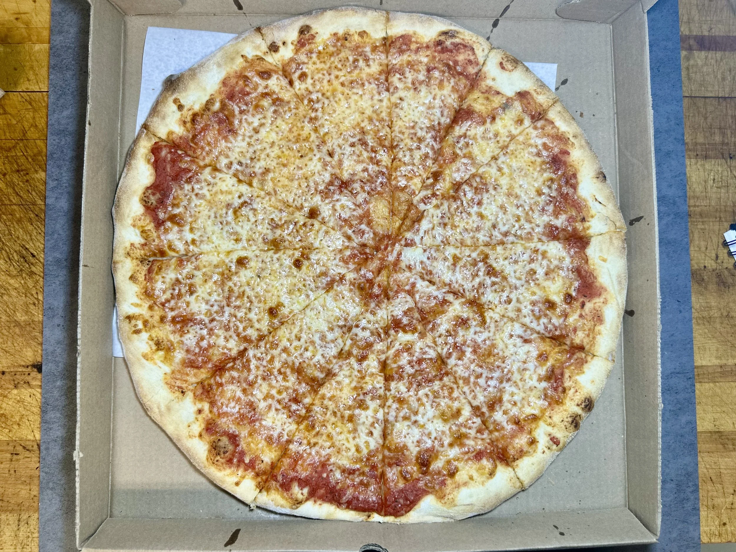A cheese pizza with sliced pieces in an open cardboard box on a wooden surface.